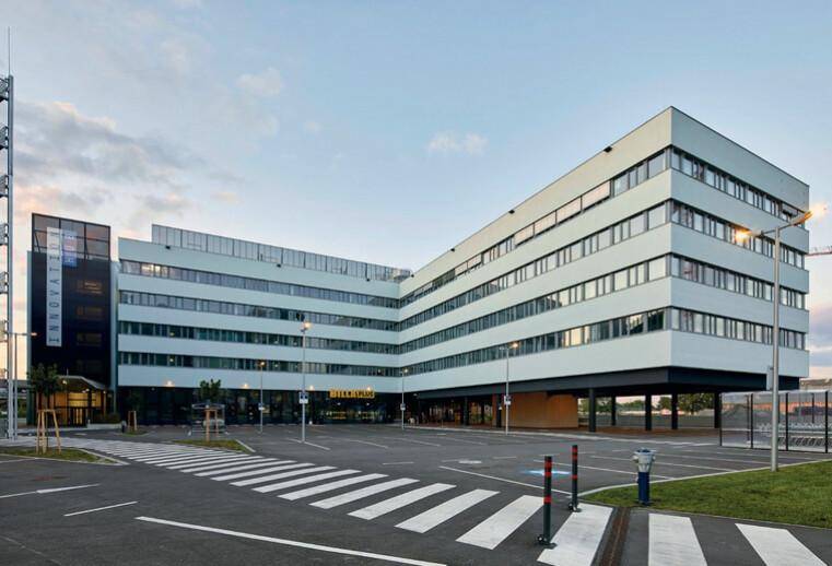 Modernes Bürogebäude mit markanter Architektur, großen Fenstern und einem Parkplatz davor.