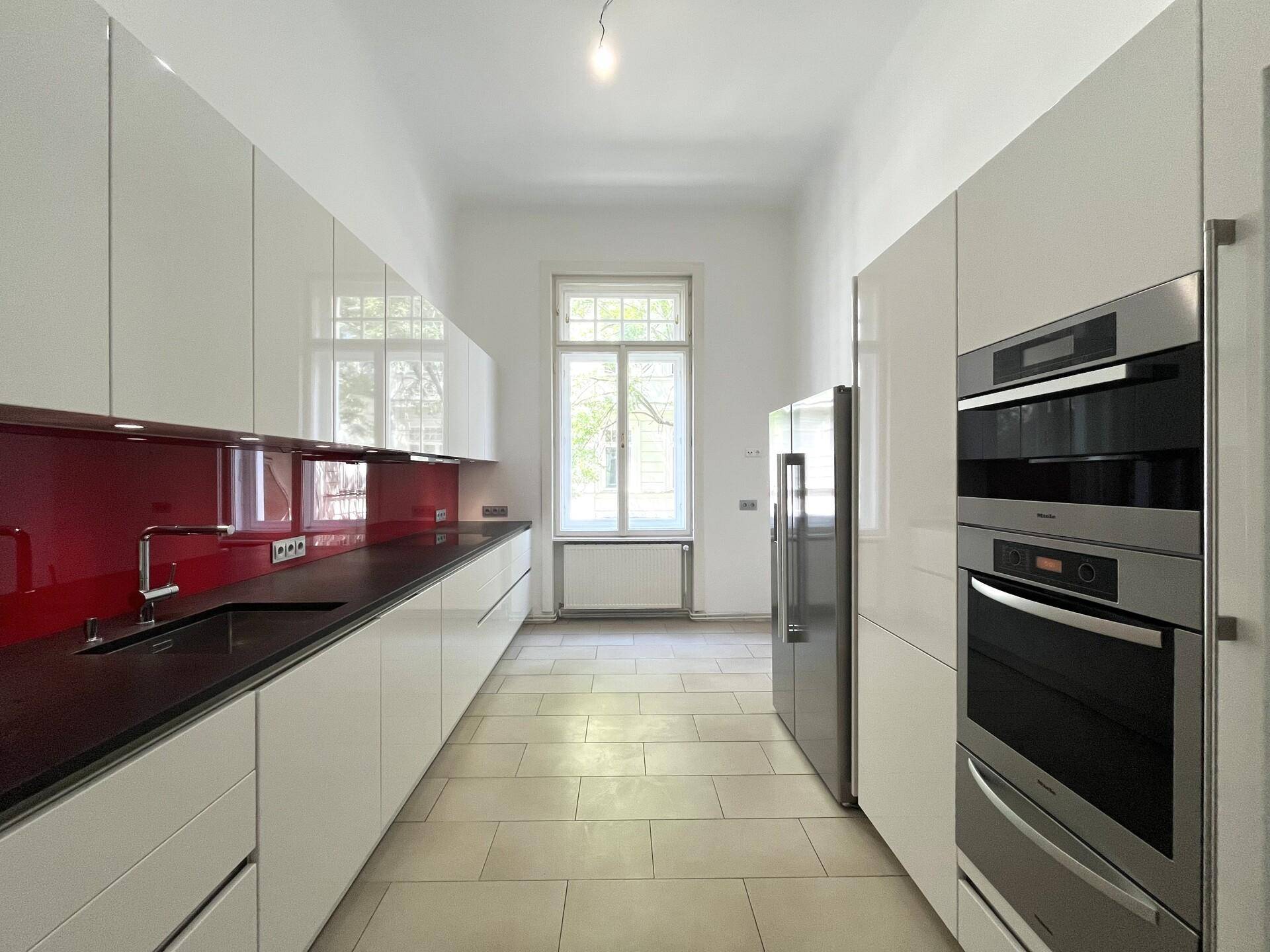 Moderne Küche mit weißen Hochglanzfronten, dunkler Arbeitsplatte und integrierten Geräten.