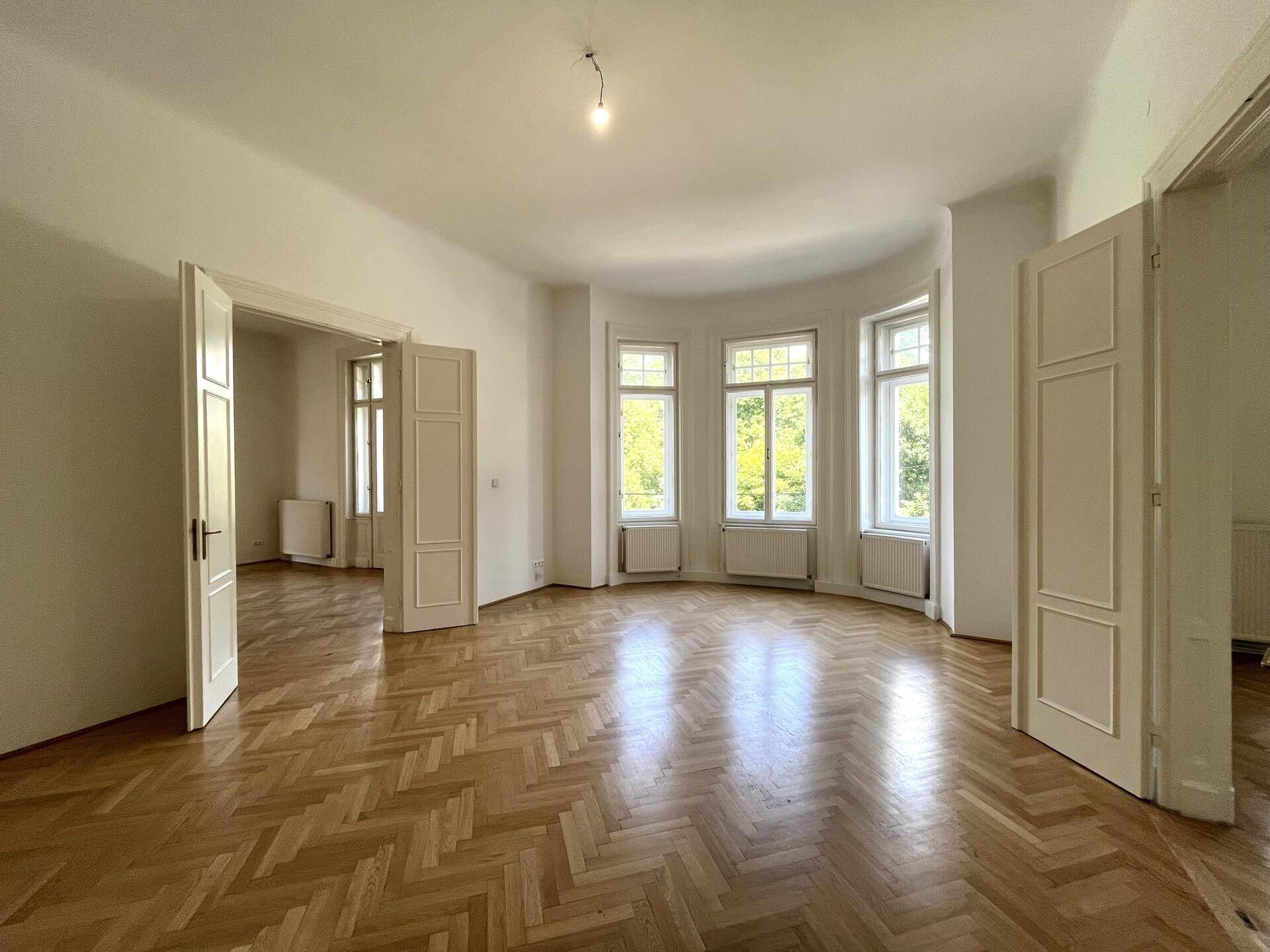 Geräumiges leeres Zimmer mit klassischem Fischgrätparkett und hellen Erkerfenstern.