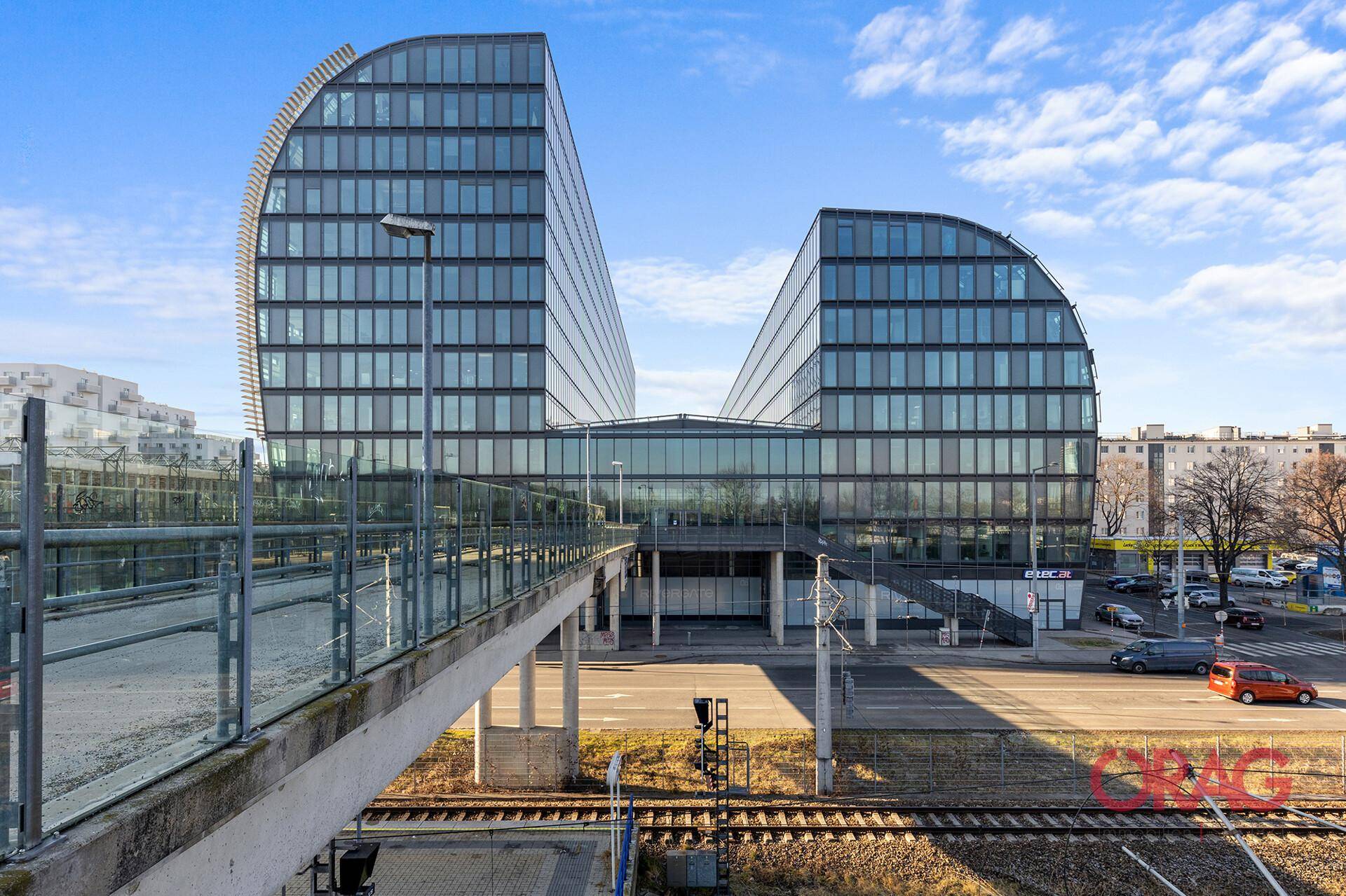 Beeindruckendes, modernes Bürogebäude mit geschwungener Glasfassade und einer Fußgängerbrücke im Vordergrund.