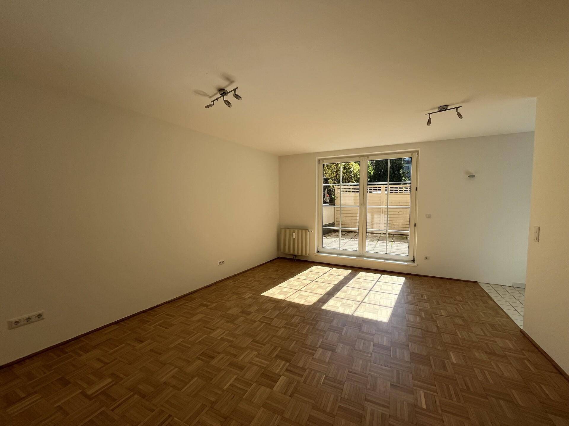 Geräumiges Wohnzimmer mit Parkettboden und großen Fenstern, die viel Tageslicht hereinlassen.