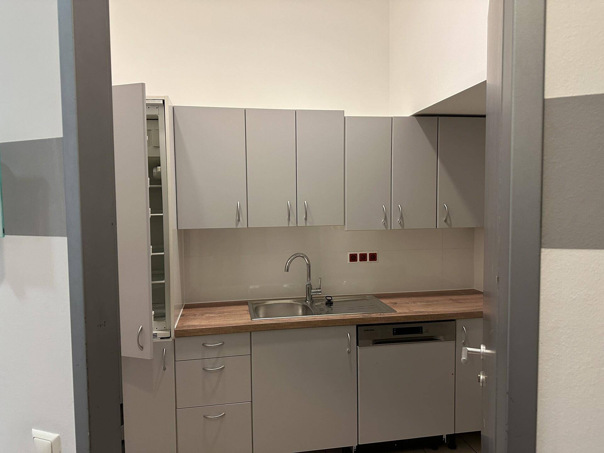 Kleine, moderne Küchenzeile mit grauen Schränken, Holztheke und Spülmaschine.