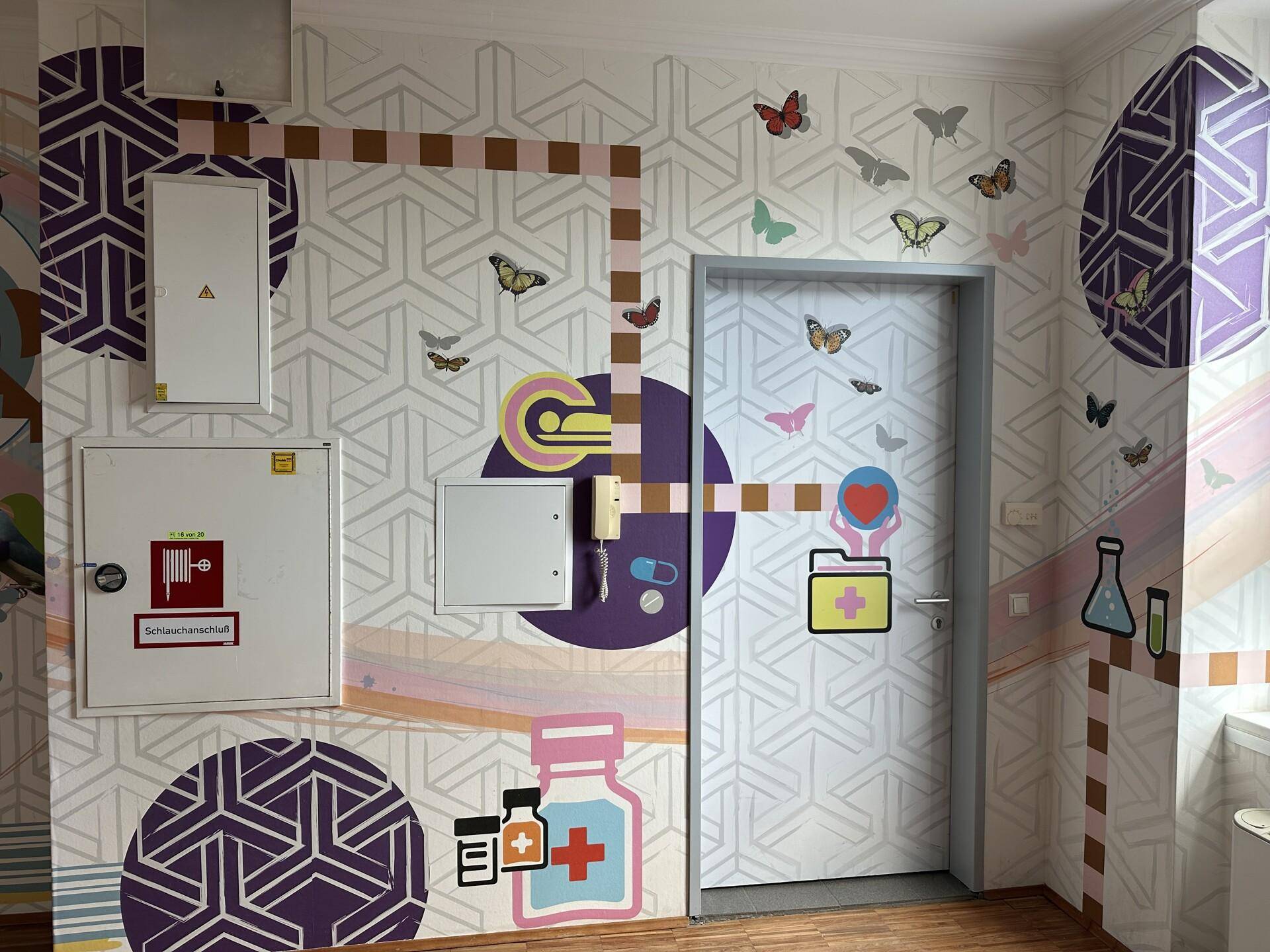Detailansicht der farbenfrohen Wandmalereien im Flur mit verschiedenen Motiven und einer Tür.