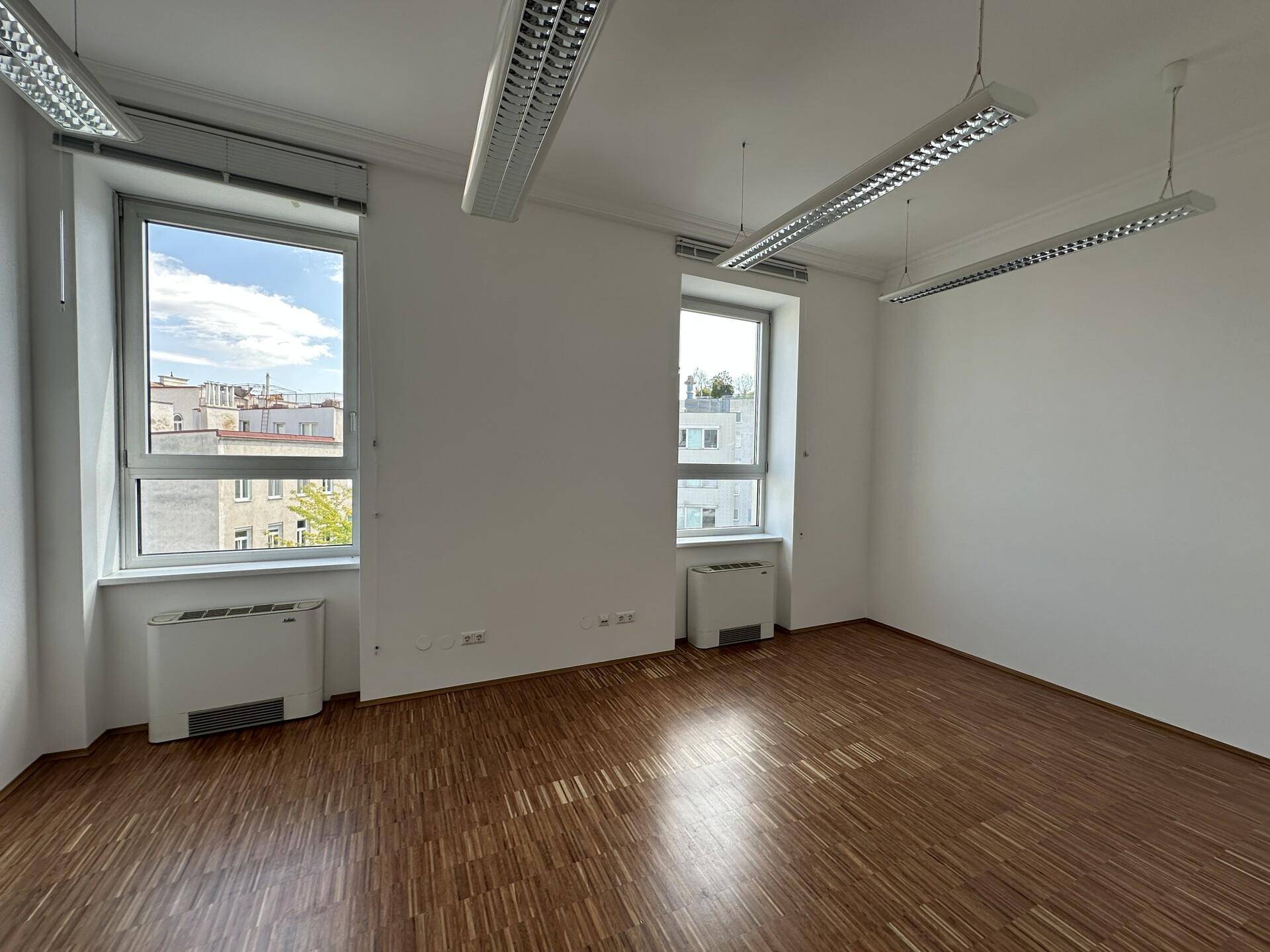 Büro mit zwei großen Fenstern, Holzboden und Klimaanlagen unter den Fenstern.