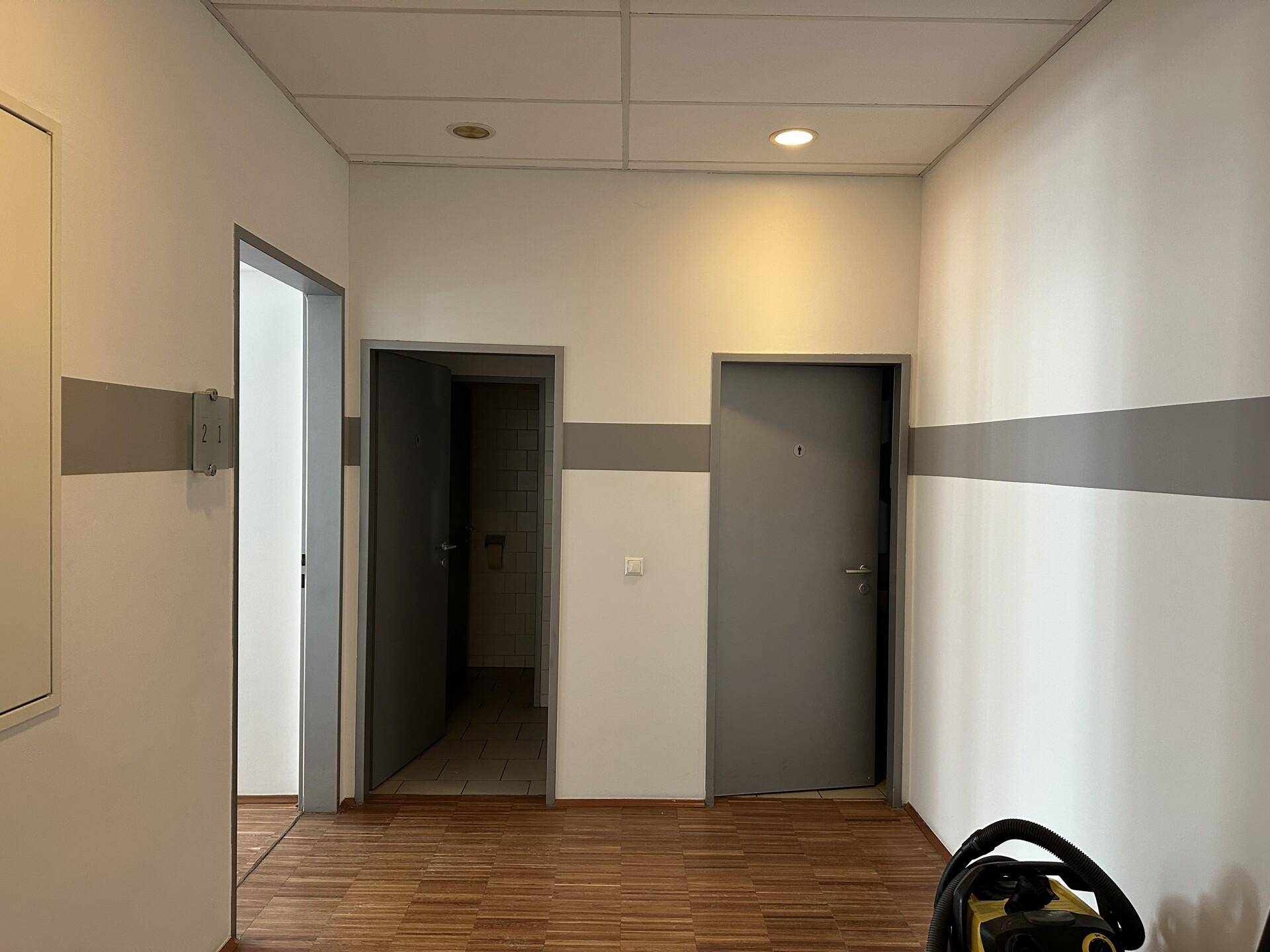 Flur mit mehreren Türen, weißen Wänden mit grauem Streifen und einer abgehängten Decke.