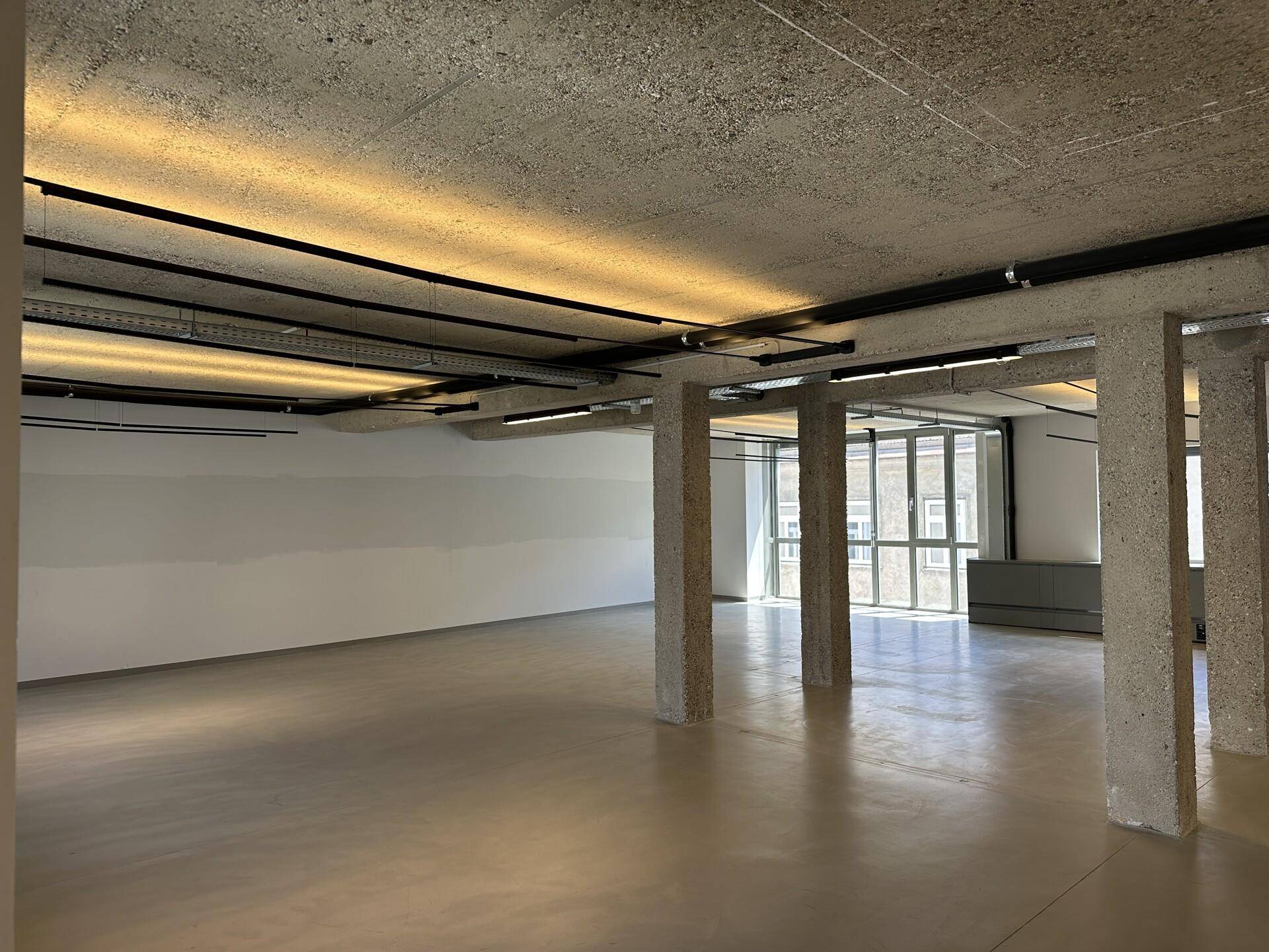 Großer, offener Büroraum mit Sichtbetondecke, Säulen und poliertem Betonboden.