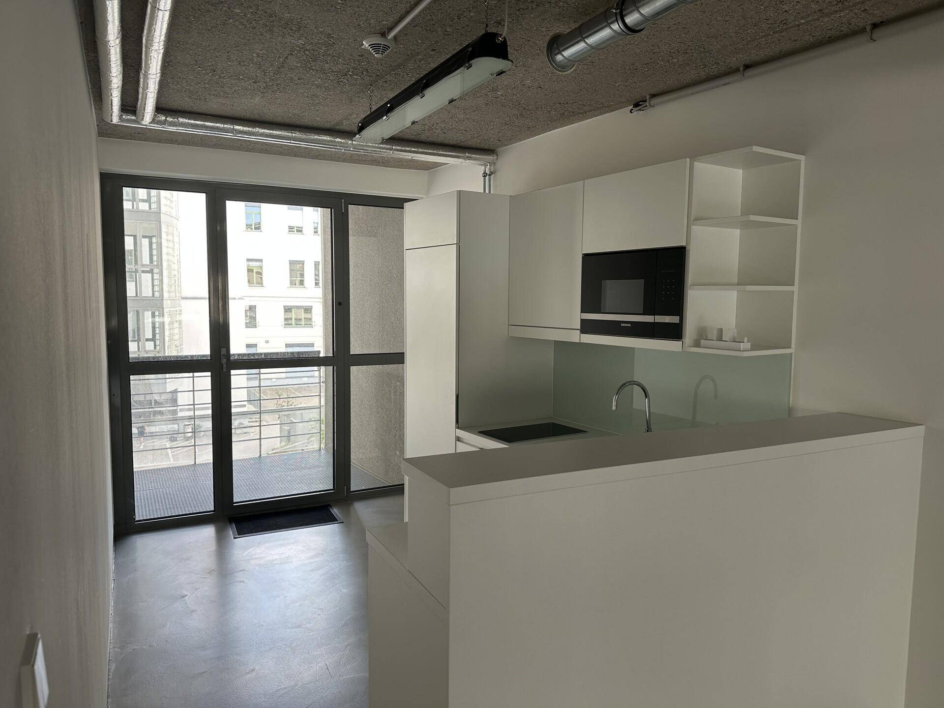 Kleine, moderne Küchenzeile mit weißen Schränken, Mikrowelle und Zugang zu einem Balkon.