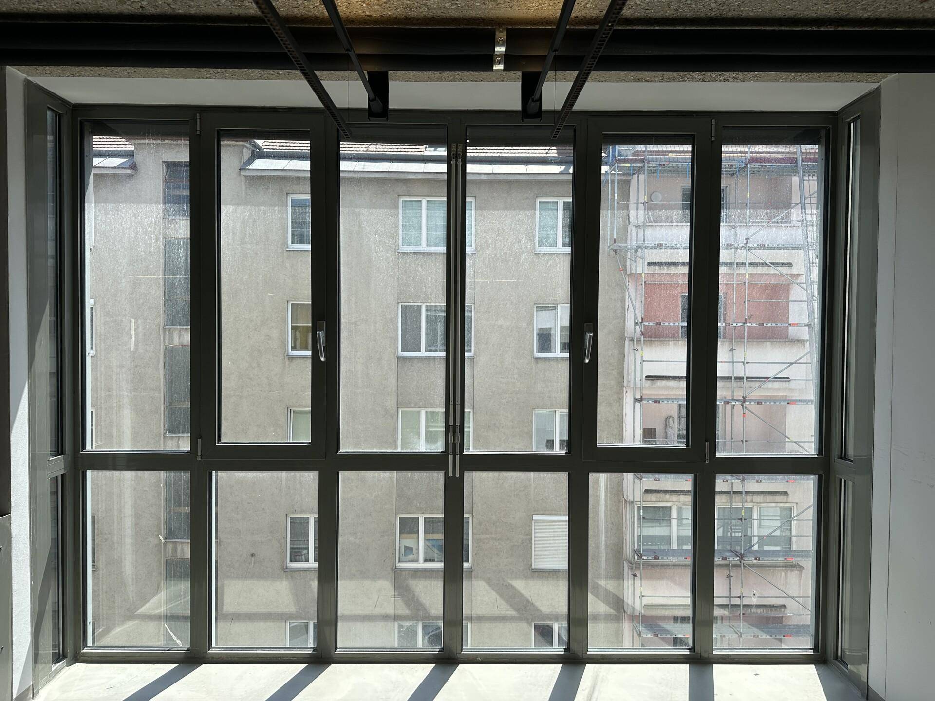 Große Fensterfront in einem Büroraum mit Blick auf gegenüberliegende Gebäude und Gerüste.