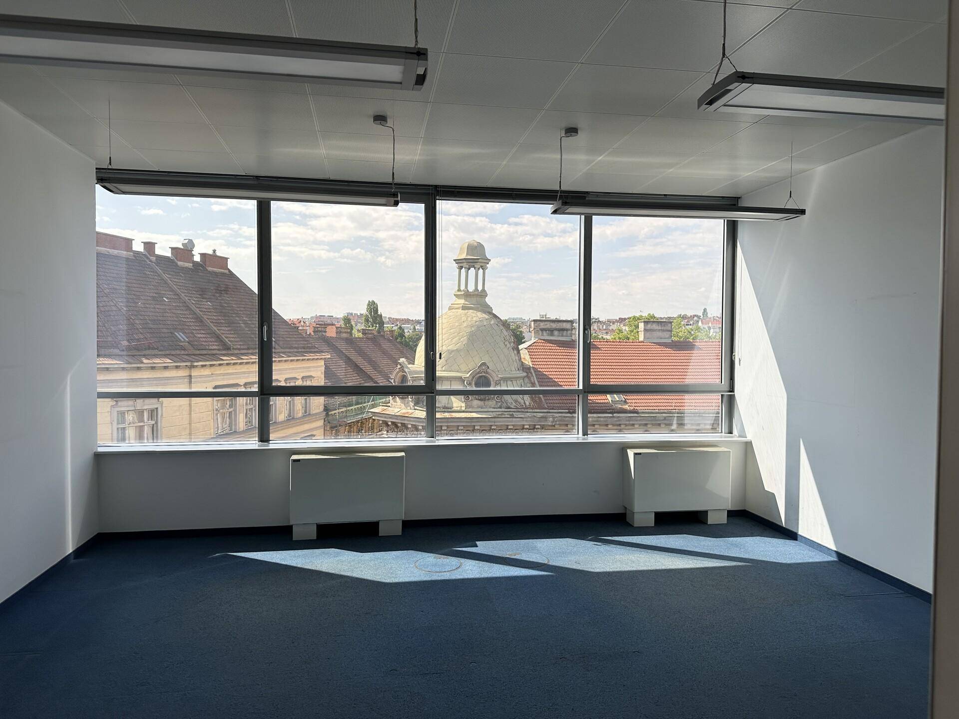 Büroraum mit weitem Ausblick auf die Stadt, inklusive historischer Kuppel, und blauem Teppichboden.