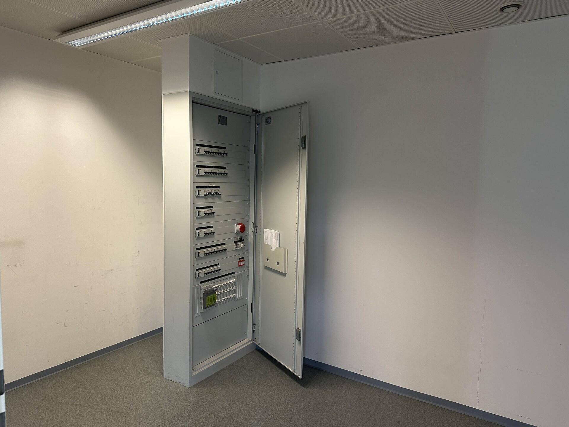 Technikraum mit offenem Sicherungskasten an der Wand und grauem Teppichboden.