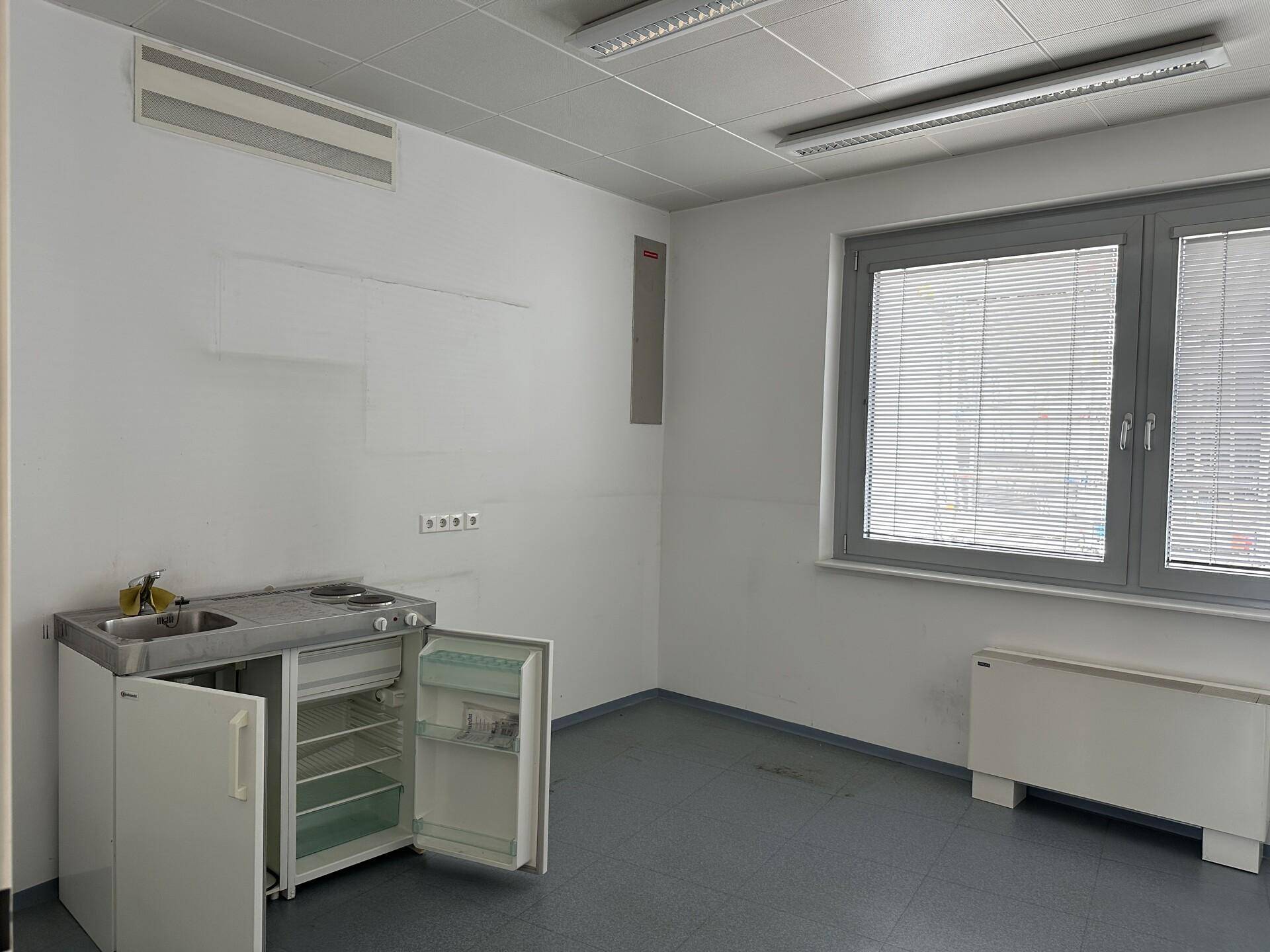 Kleiner Raum mit einfacher Küchenzeile, Fenster mit Jalousien und Klimaanlage.