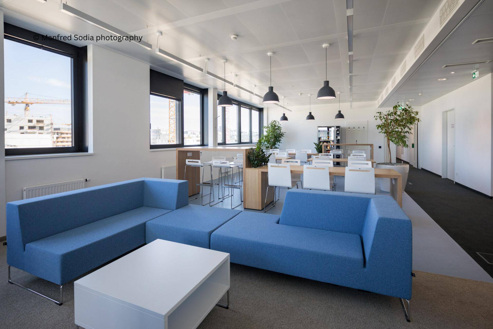 Helle Lounge mit blauen Sofas, einem weißen Couchtisch und einem Essbereich im Hintergrund.