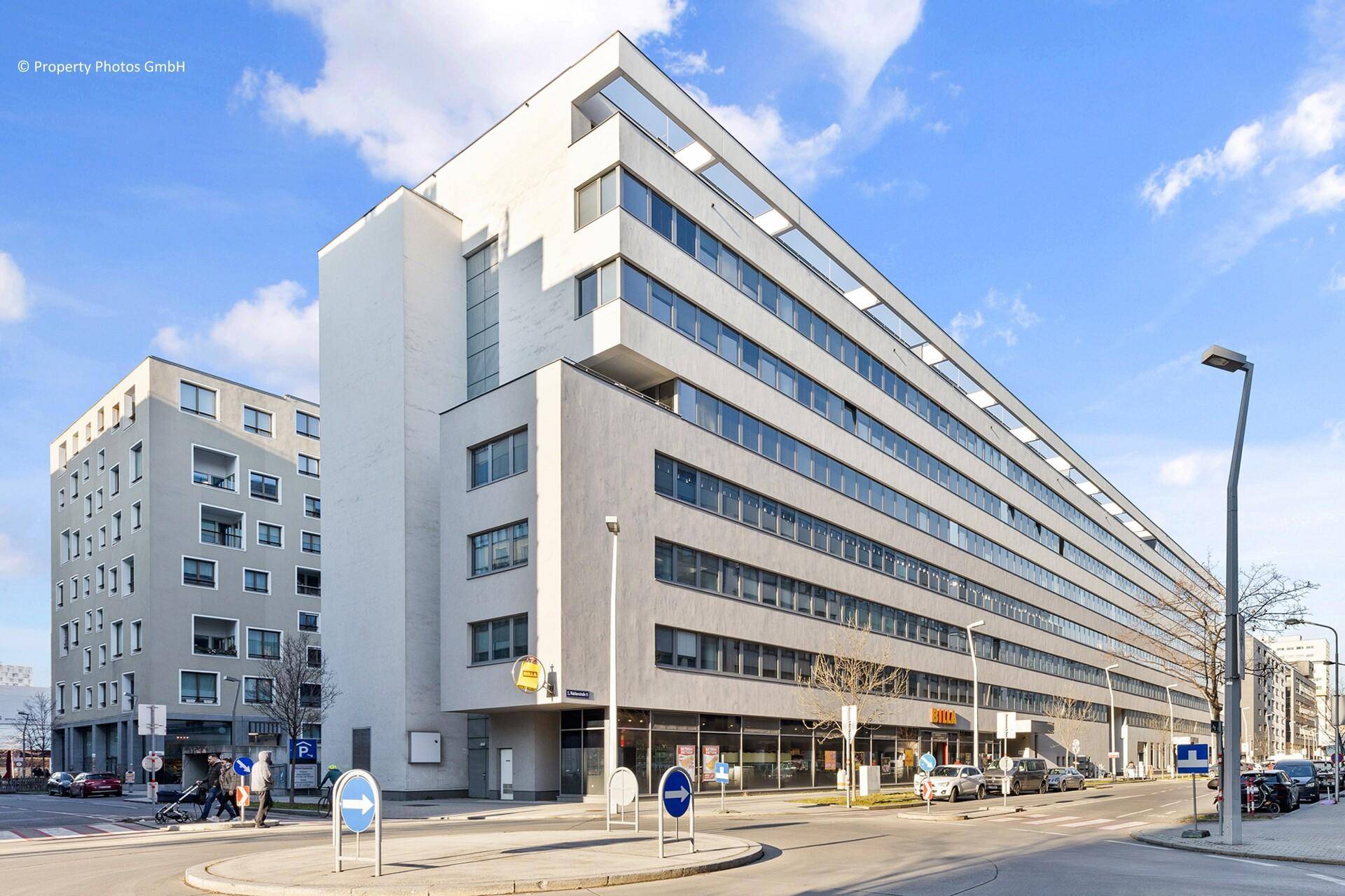 Modernes Geschäftsgebäude mit vielen Fenstern und klaren Linien an einer städtischen Straße.