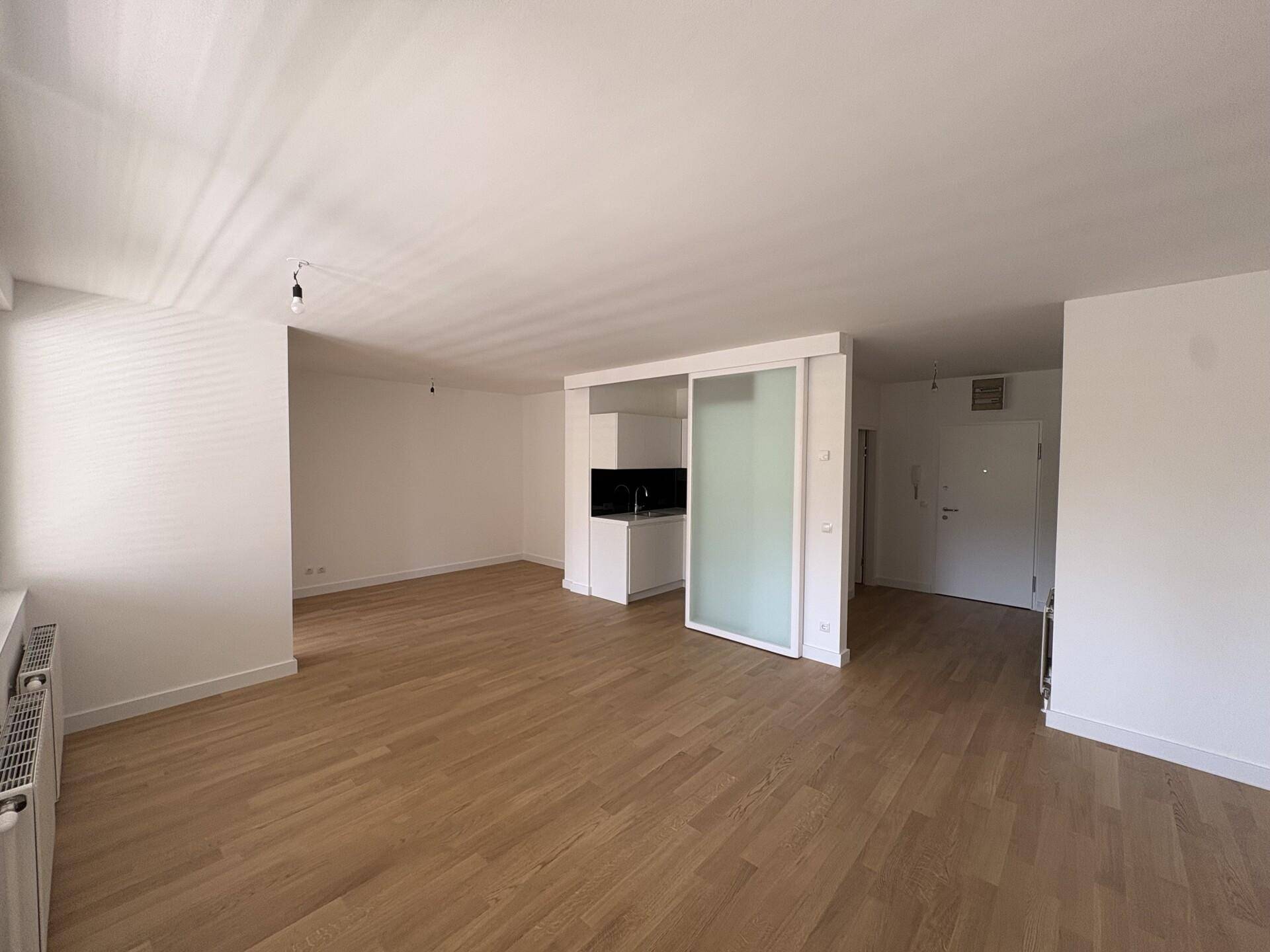Geräumiges Wohnzimmer mit Parkettboden und Zugang zu einer modernen Kochnische.