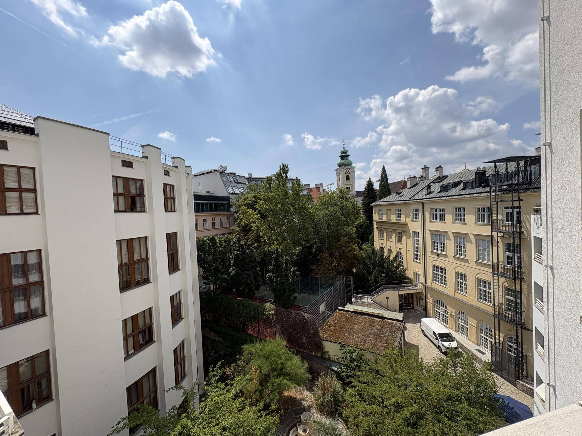 Panoramablick über die Stadt mit grünen Bäumen, historischen Gebäuden und einem Kirchturm.