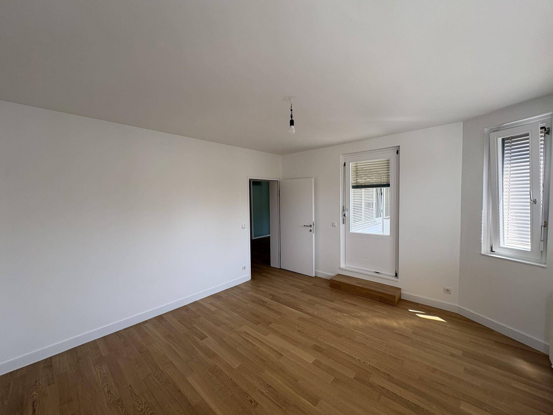 Schlafzimmer mit Parkettboden, weißen Wänden und Zugang zu einem Außenbereich.