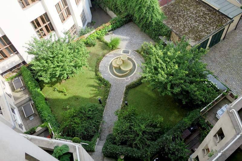 Weitläufiger Blick auf den grünen Innenhofgarten mit Brunnen, umgeben von Gebäuden.