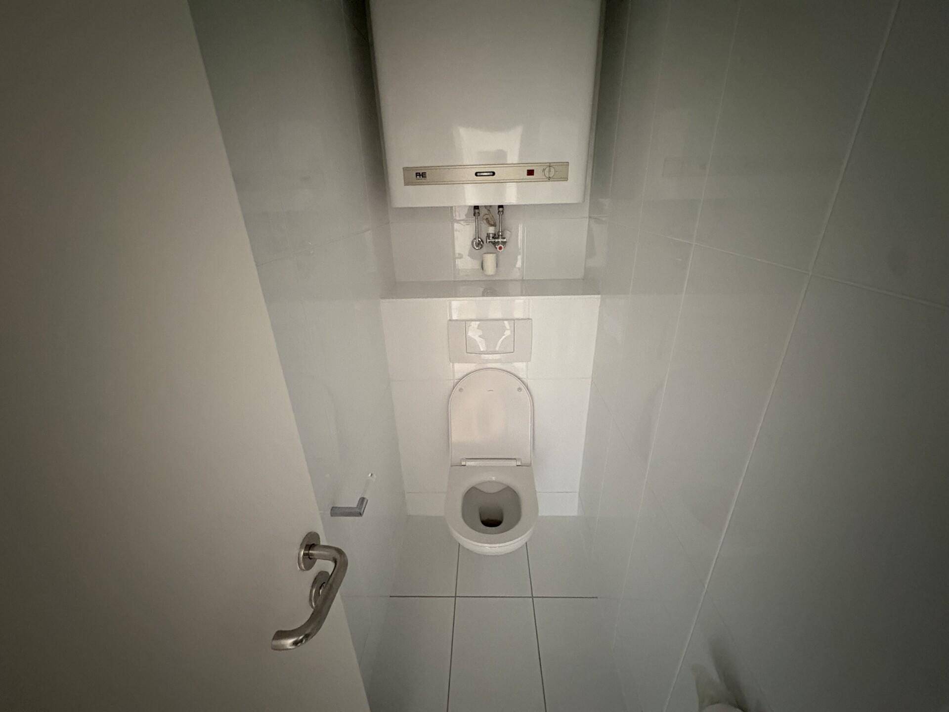 Separates WC mit weißer Toilette und hellen Fliesen an Wänden und Boden.