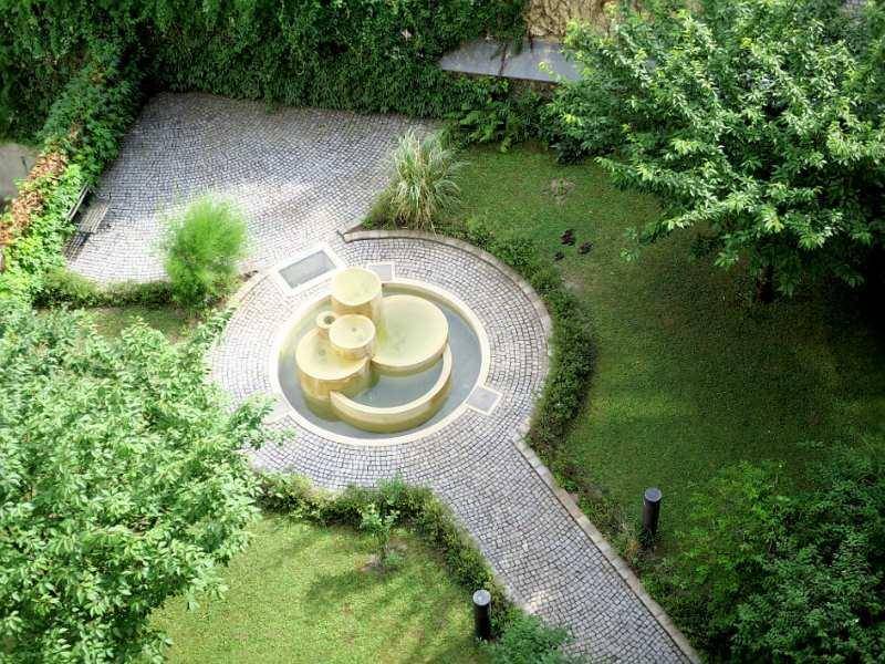 Gepflegter Innenhofgarten mit einem dekorativen Brunnen, Rasenflächen und gepflasterten Wegen.