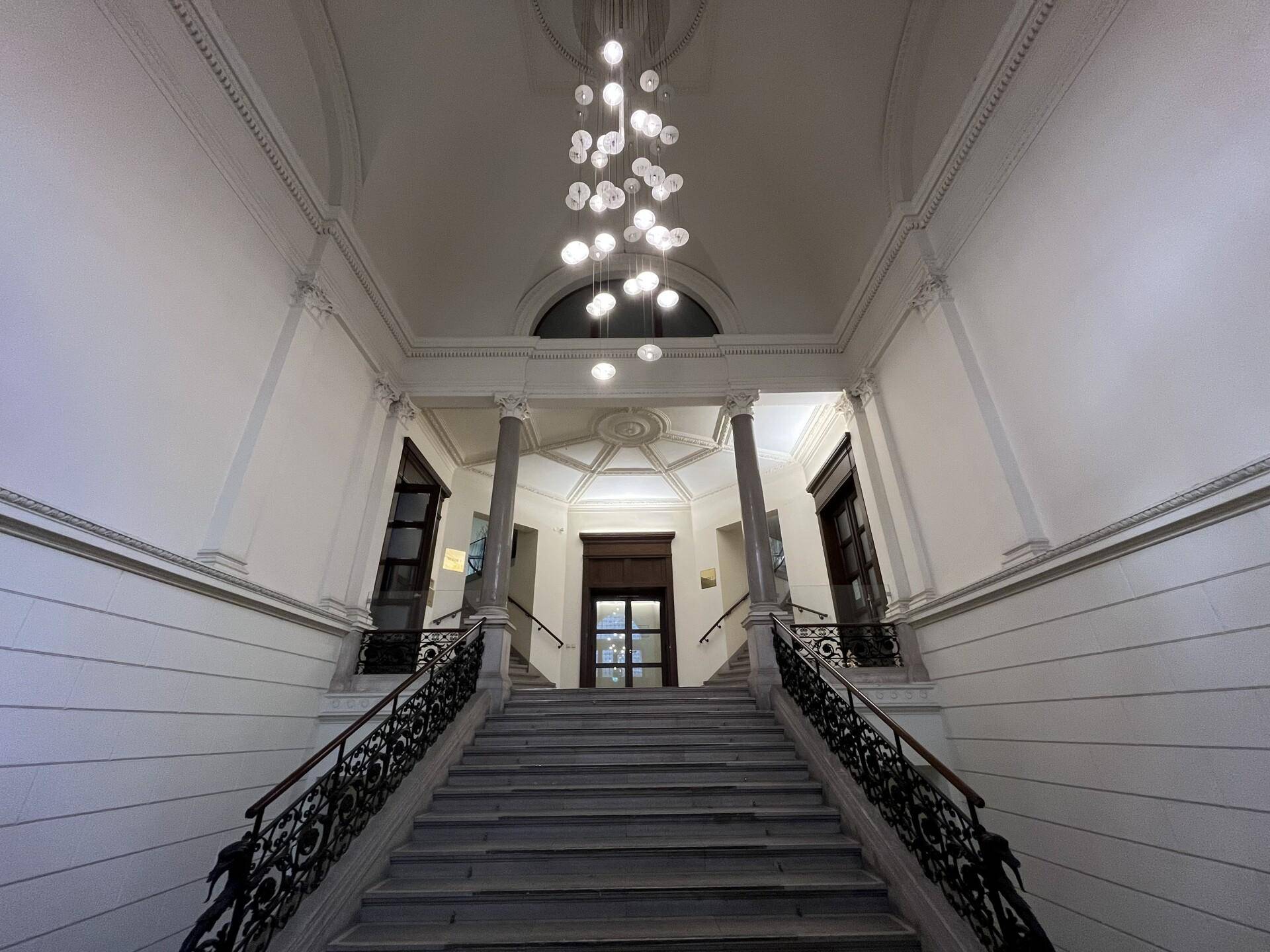 Prächtiges Treppenhaus mit hohen Decken, elegantem Kronleuchter und kunstvollem Geländer.