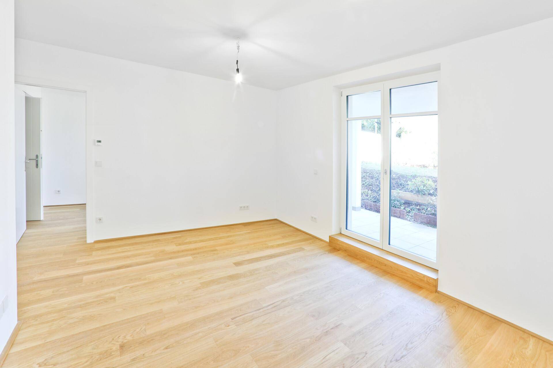 Lichtdurchfluteter Wohnraum mit hellem Holzboden und Blick ins Grüne.