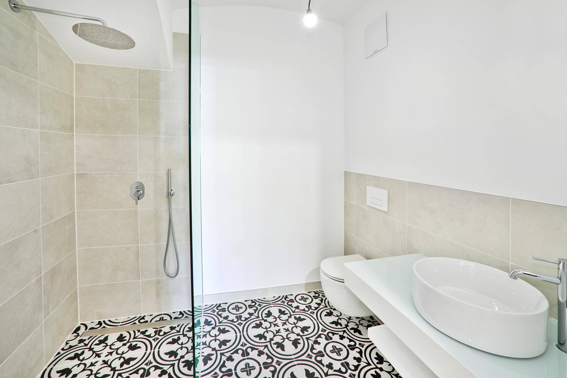 Modernes Badezimmer mit begehbarer Dusche, Aufsatzwaschbecken und gemusterten Bodenfliesen.