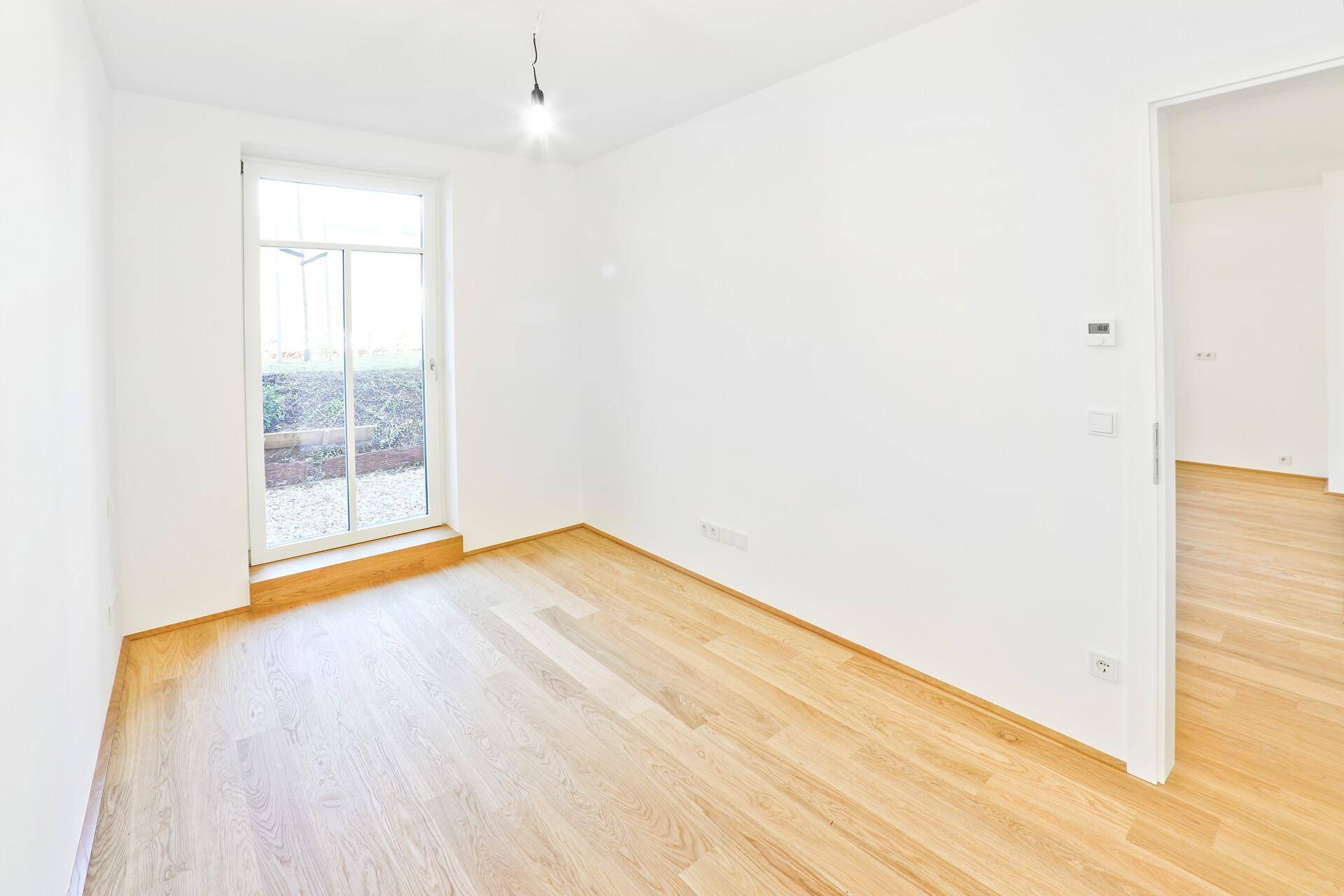 Heller Raum mit Holzboden und großem Fenster, ideal als Schlaf- oder Arbeitszimmer.