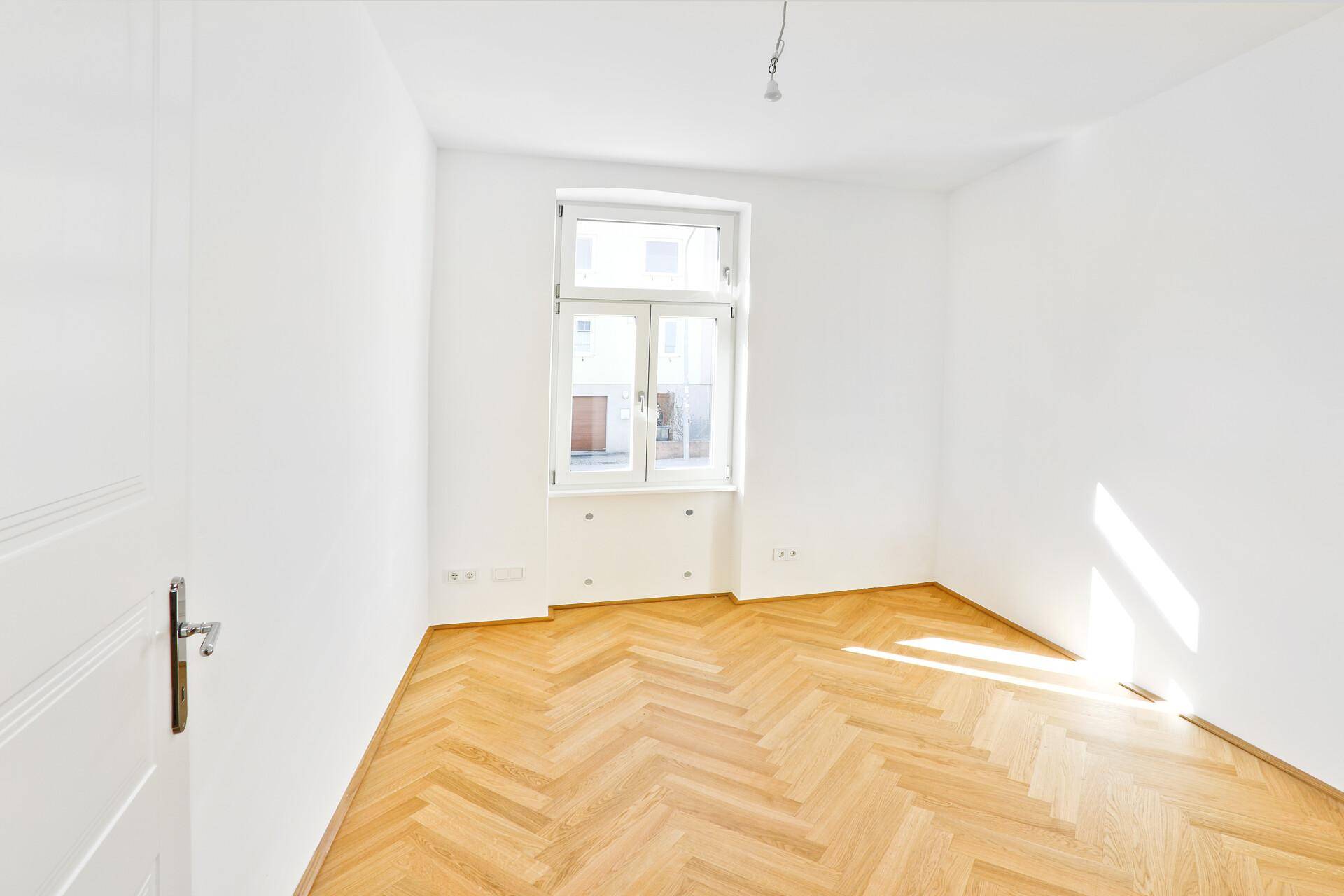 Gemütliches Schlafzimmer mit klassischem Fischgrätparkett und einem Fenster für natürliches Licht.