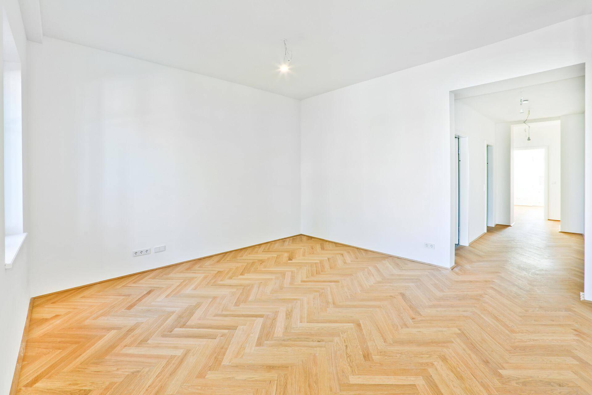 Geräumiges Zimmer mit hellem Fischgrätparkett und weiß gestrichenen Wänden, ideal für Wohnzwecke.