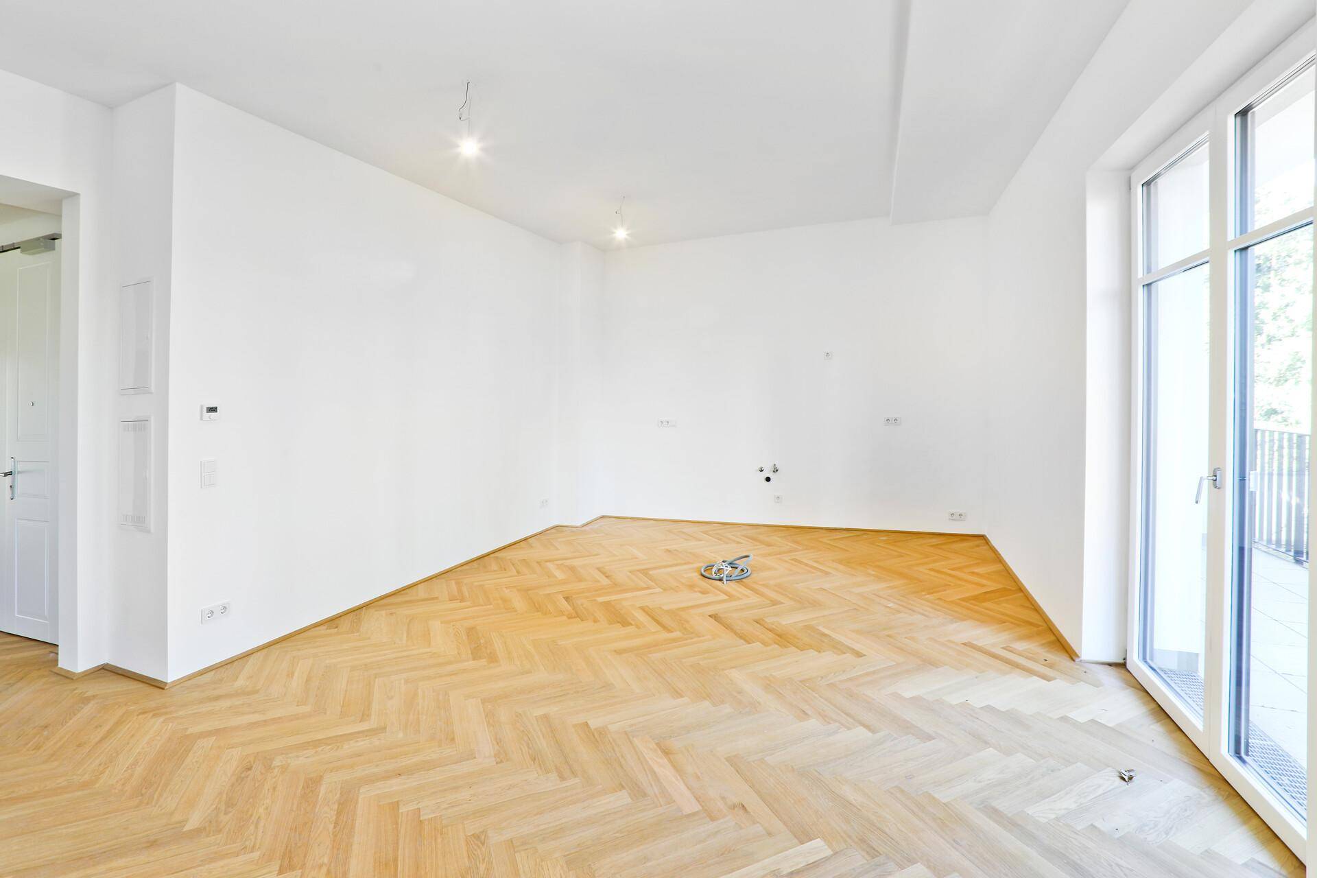 Großzügiges Zimmer mit Fischgrätparkett und viel Tageslicht durch die breite Balkontür.