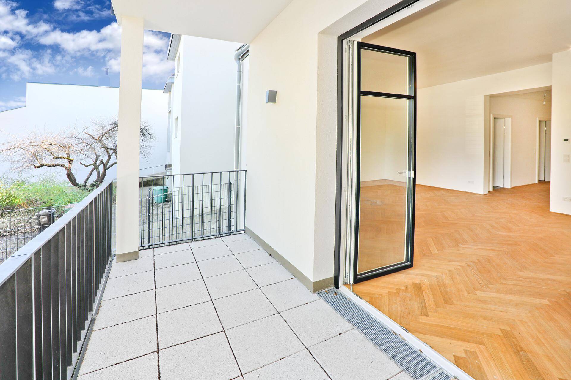 Heller Balkon mit Fliesenboden und Zugang zu einem Zimmer mit Fischgrätparkett.