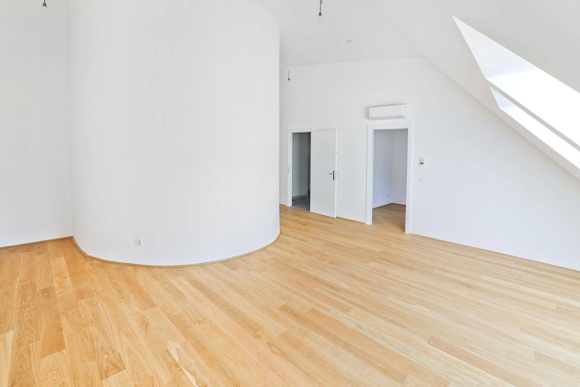 Großer, heller Raum mit Holzparkettboden, einer runden Wand und Dachschräge.