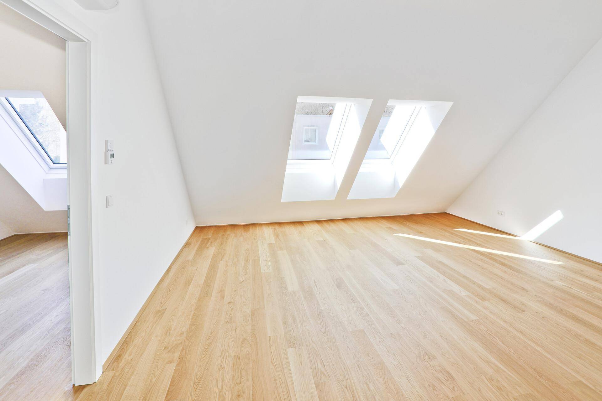 Lichtdurchfluteter Raum mit Holzparkett, zwei Dachfenstern und ausgeprägter Dachschräge.