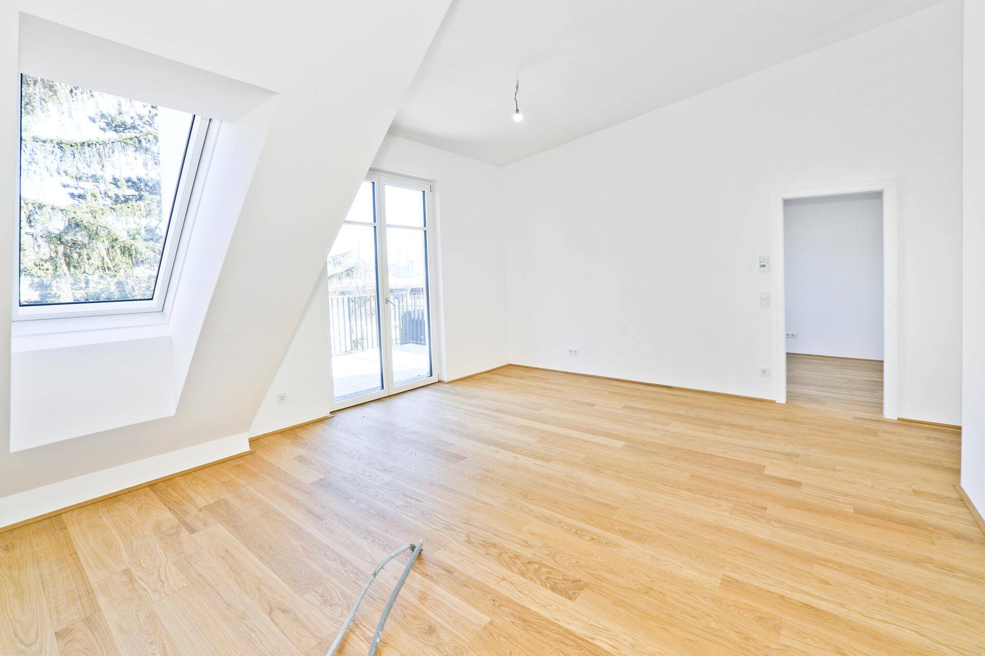 Geräumiger, heller Raum mit Holzparkett, Dachfenster und direktem Balkonzugang.