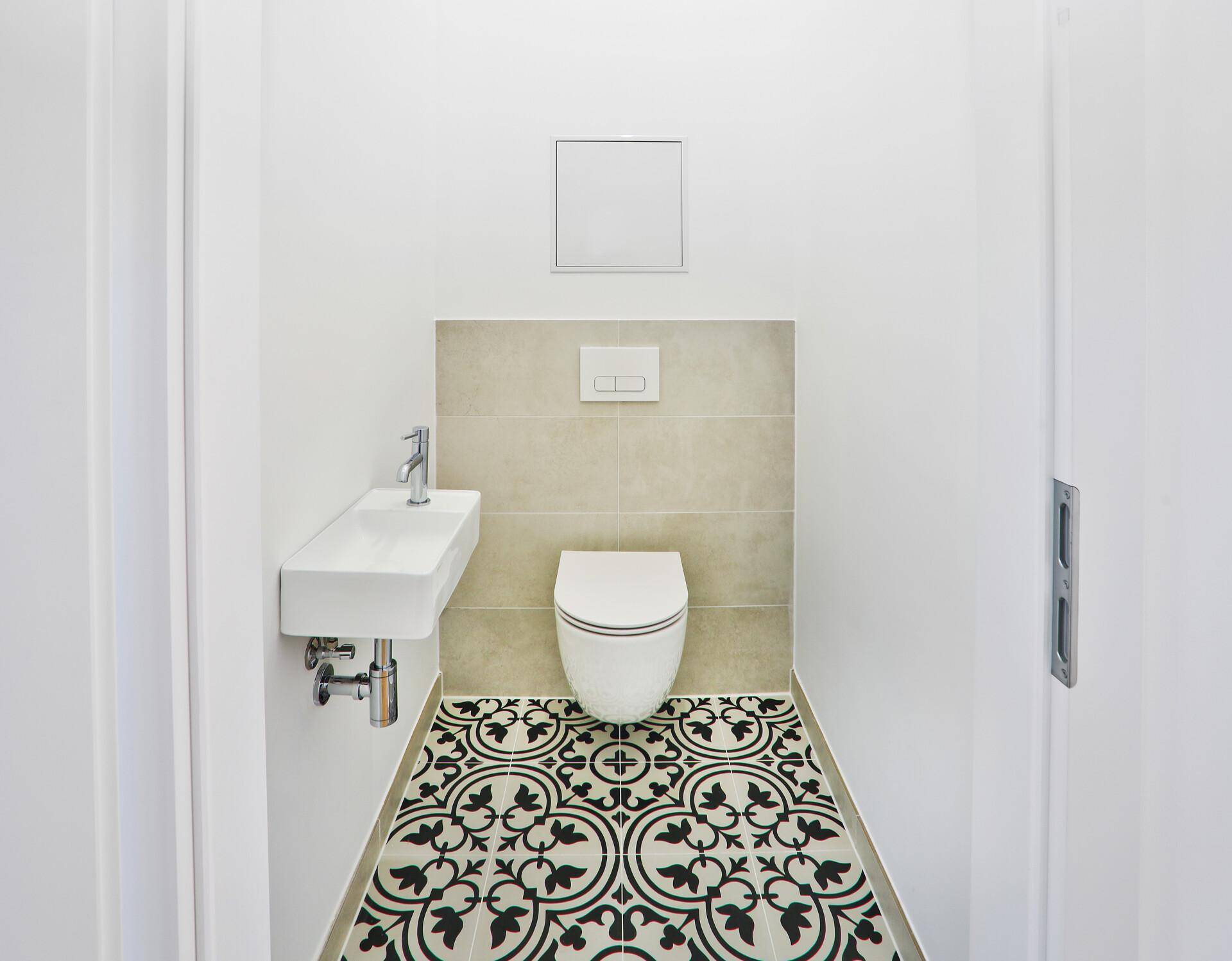 Modernes Gäste-WC mit Wand-WC, kleinem Waschbecken und dekorativem Fliesenboden.