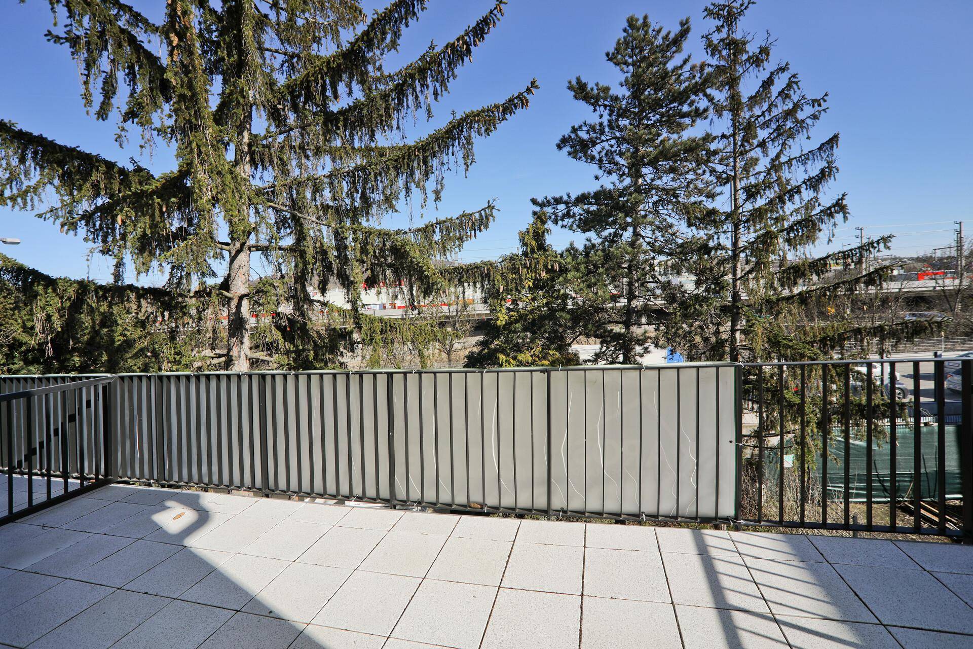 Geräumiger Balkon mit Fliesenboden und Blick auf hohe Bäume und die umliegende Landschaft.