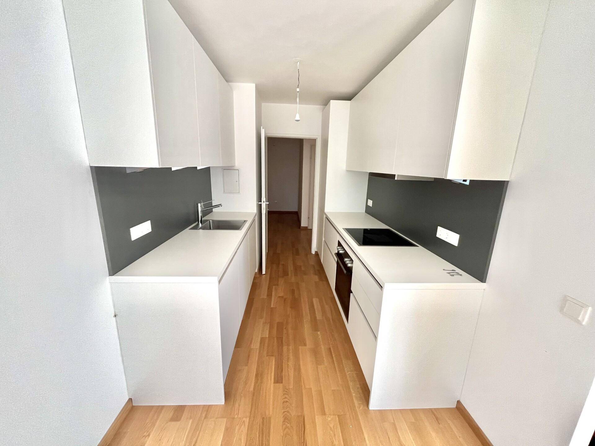 Moderne, schmale Einbauküche mit weißen Fronten, dunkler Rückwand und Holzboden.