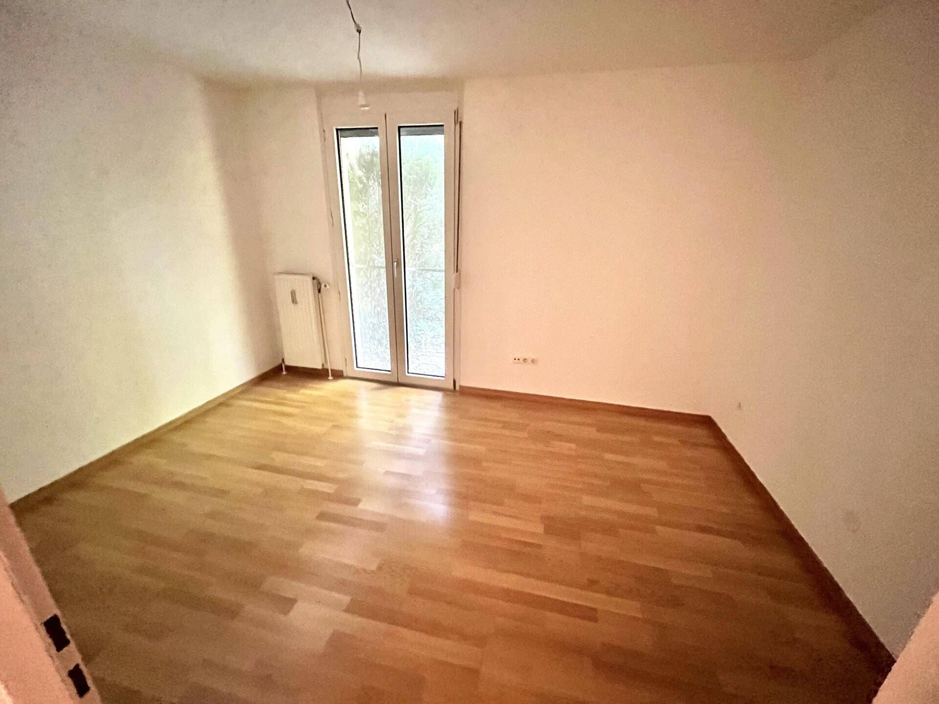Helles Schlafzimmer mit Parkettboden und Zugang zu einem Balkon oder einer Terrasse.