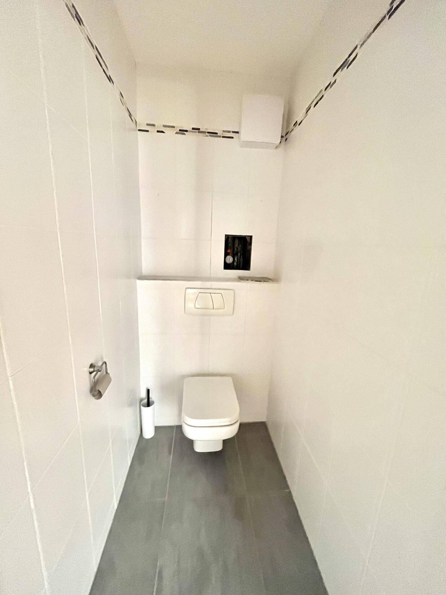 Modernes Gäste-WC mit weißen Wandfliesen, grauem Boden und wandhängendem WC.