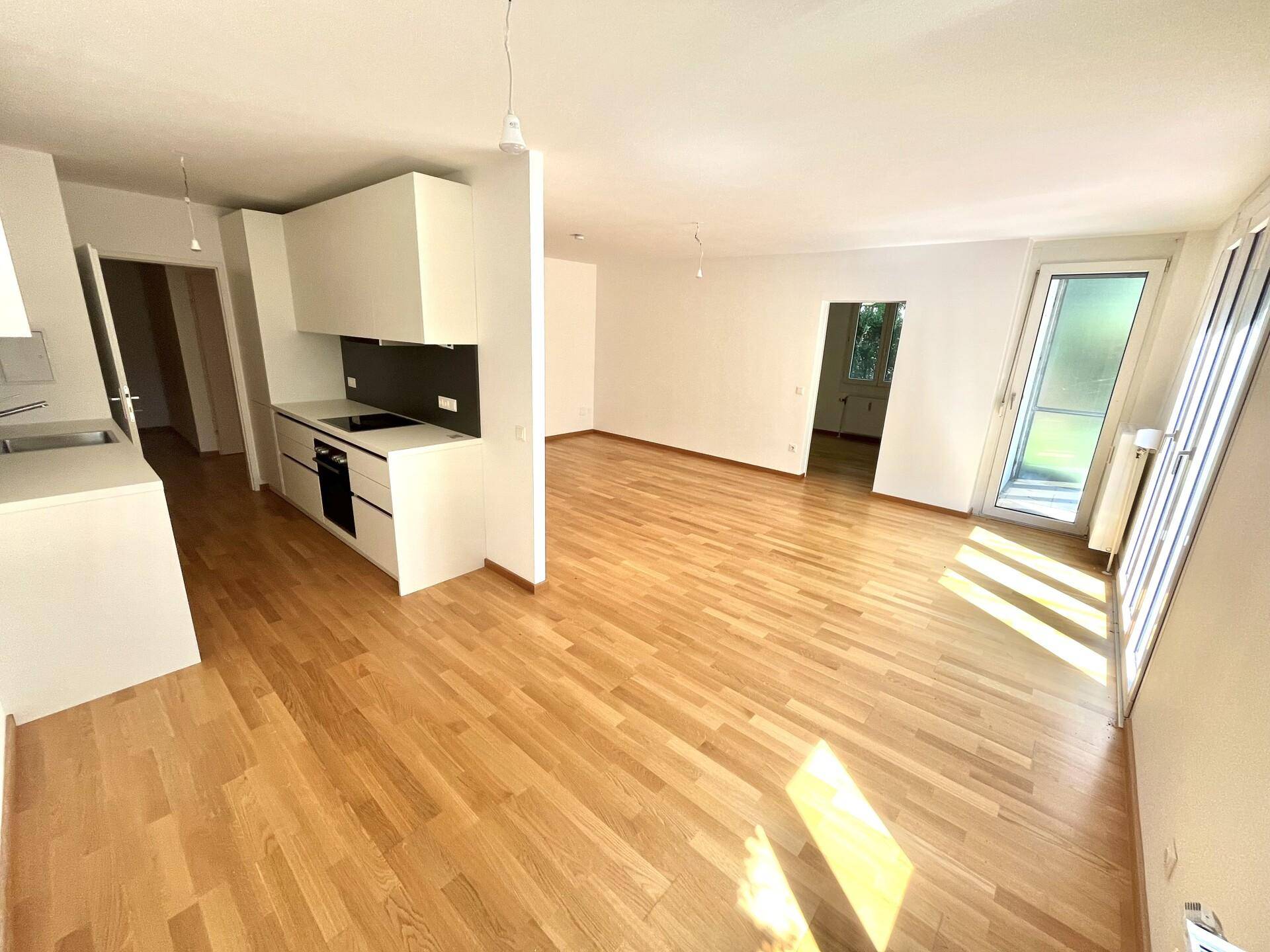 Lichtdurchfluteter Wohnbereich mit Parkettboden, großen Fenstern und moderner Küchenzeile.