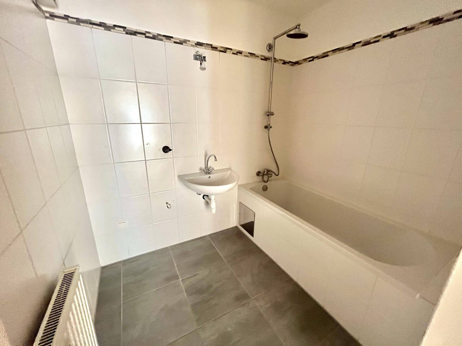 Badezimmer mit Badewanne, integrierter Dusche, Waschbecken und grauen Bodenfliesen.