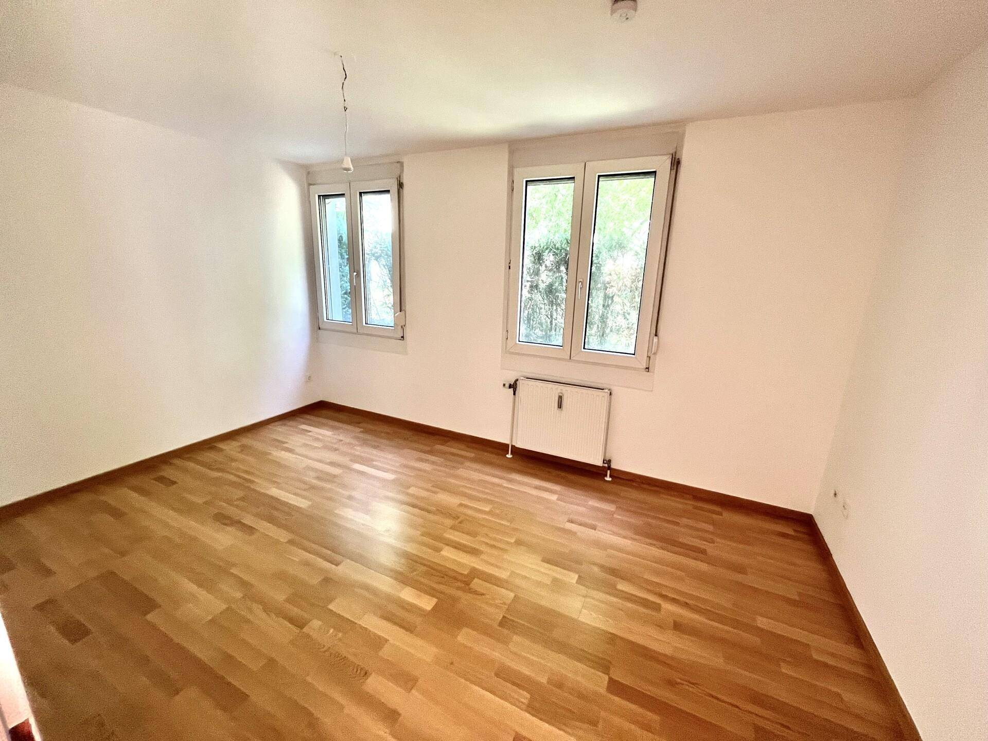Geräumiges, helles Schlafzimmer mit Parkettboden und zwei großen Fenstern mit Grünblick.
