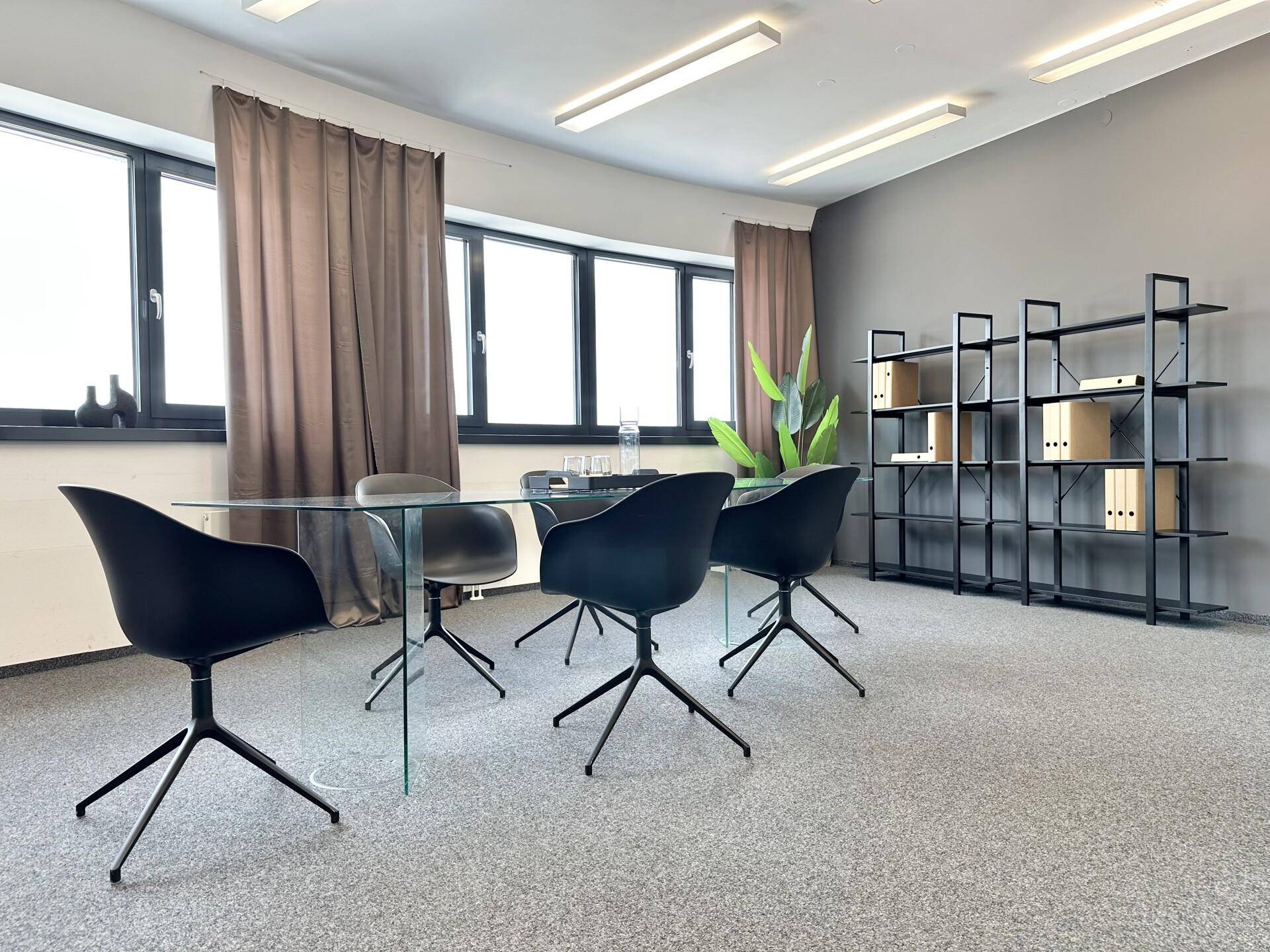 Konferenzraum mit modernem Glastisch, schwarzen Stühlen und Regalen, bietet eine professionelle Arbeitsumgebung.