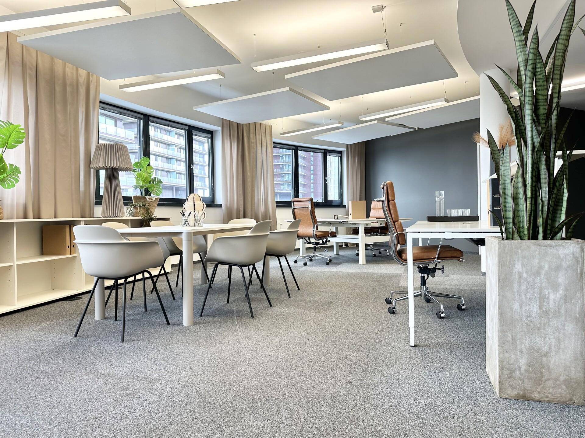 Großzügiges, modernes Büro mit Teppichboden, mehreren Arbeitsbereichen und schallabsorbierenden Deckenplatten.