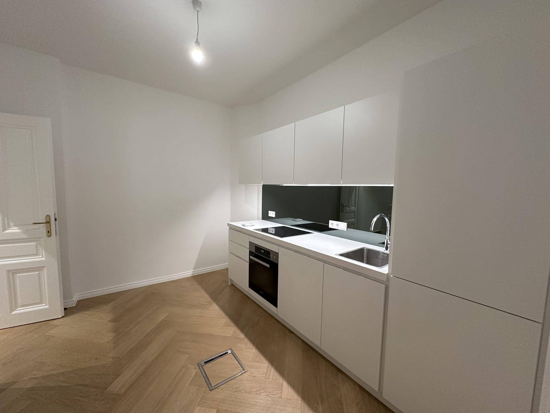 Moderne, kompakte Küche mit weißen Schränken, integrierten Geräten und elegantem Fischgrätparkett.