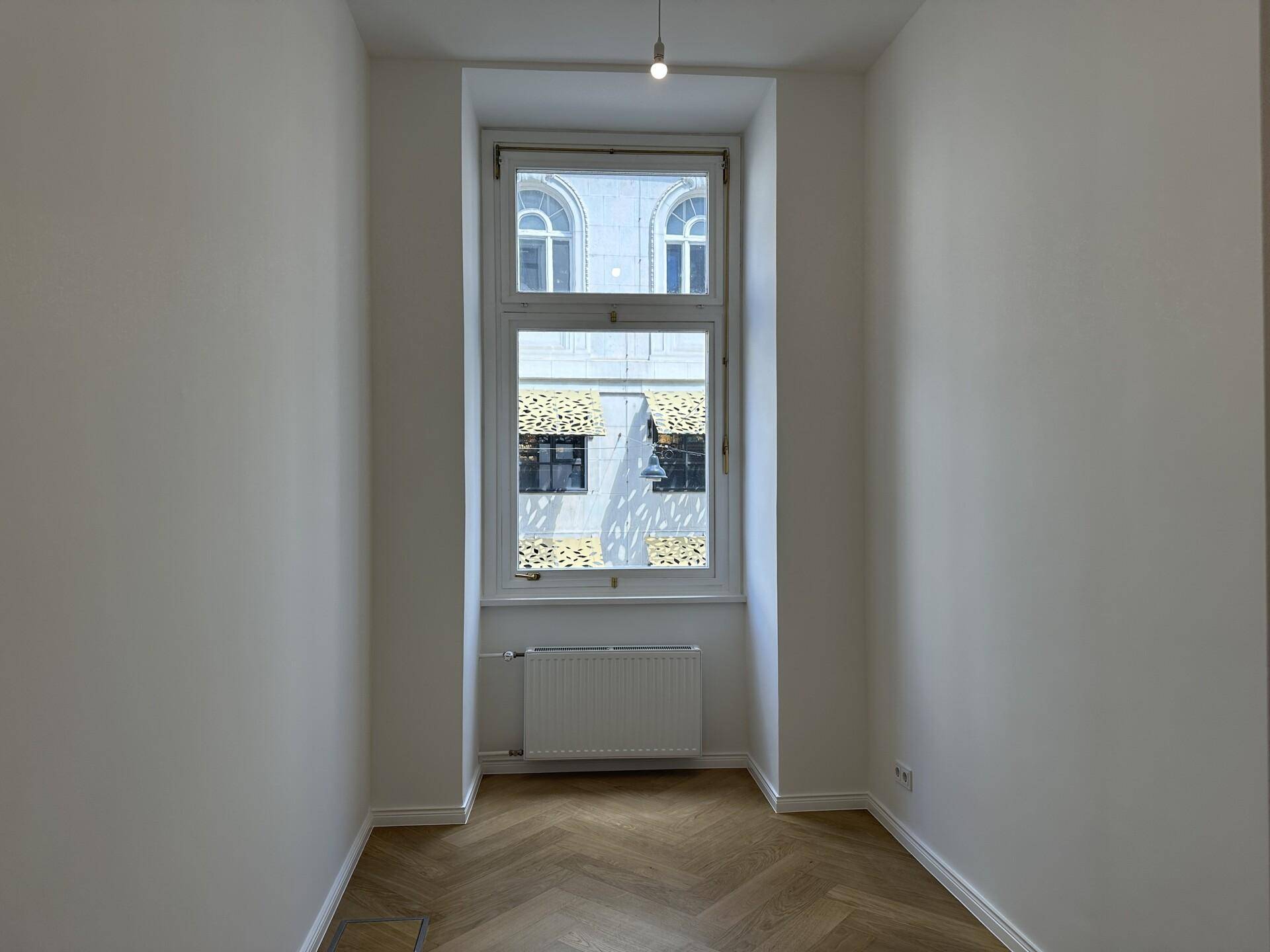 Helles Zimmer mit hohem Fenster, Fischgrätparkett und weiß gestrichenen Wänden, bietet vielseitige Nutzungsmöglichkeiten.