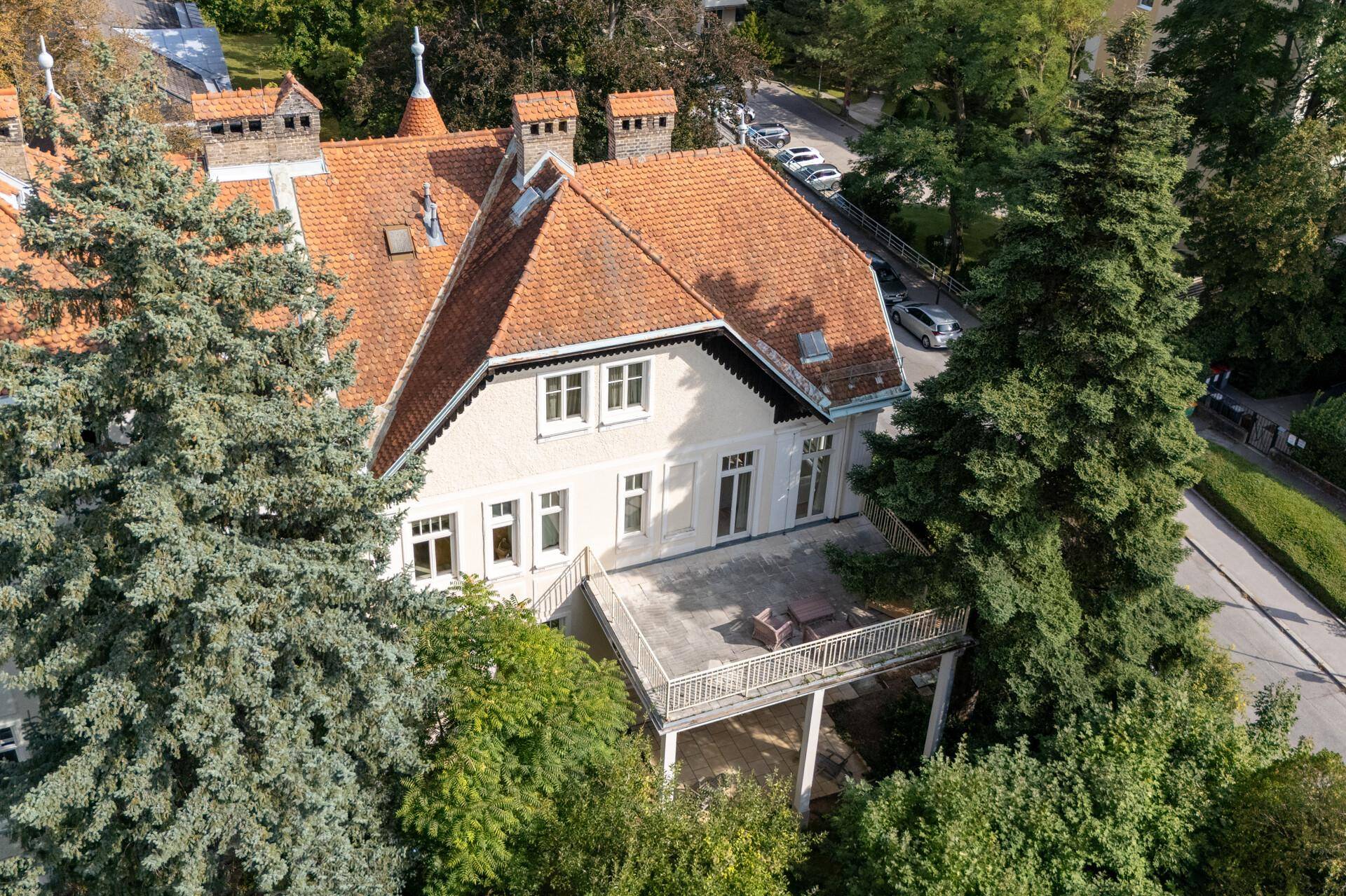 Dachansicht der Villa mit großer Terrasse und Sitzgelegenheiten, umgeben von hohen Bäumen.