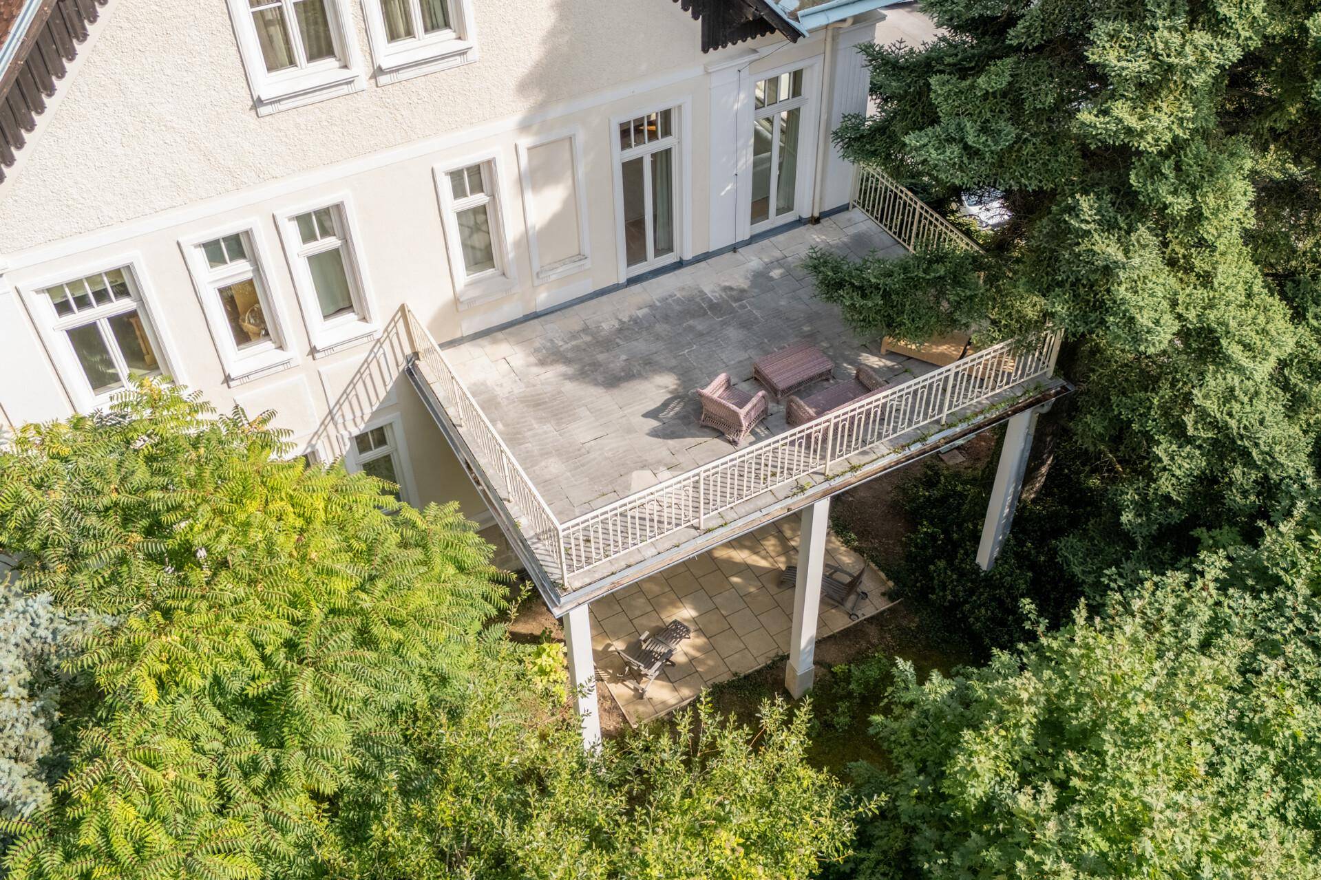 Große Steinterrasse mit Sitzgelegenheiten, umgeben von Bäumen und mit Blick ins Grüne.