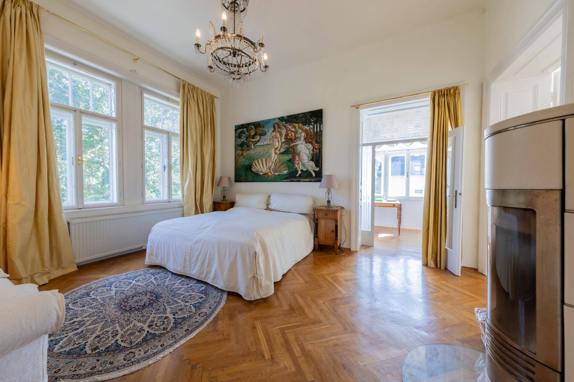 Helles Schlafzimmer mit Parkettboden, Kamin und Zugang zu einem weiteren Raum.