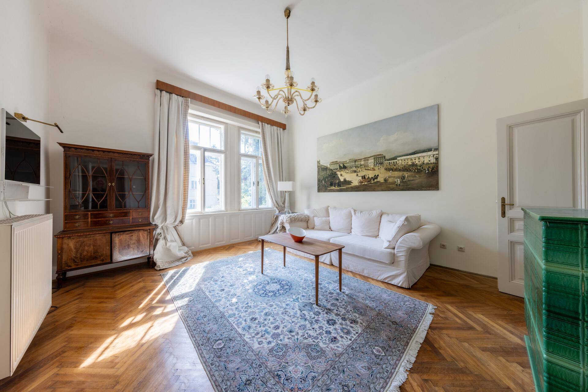 Gemütliches Wohnzimmer mit Parkettboden, großem Fenster und traditionellem Kachelofen.